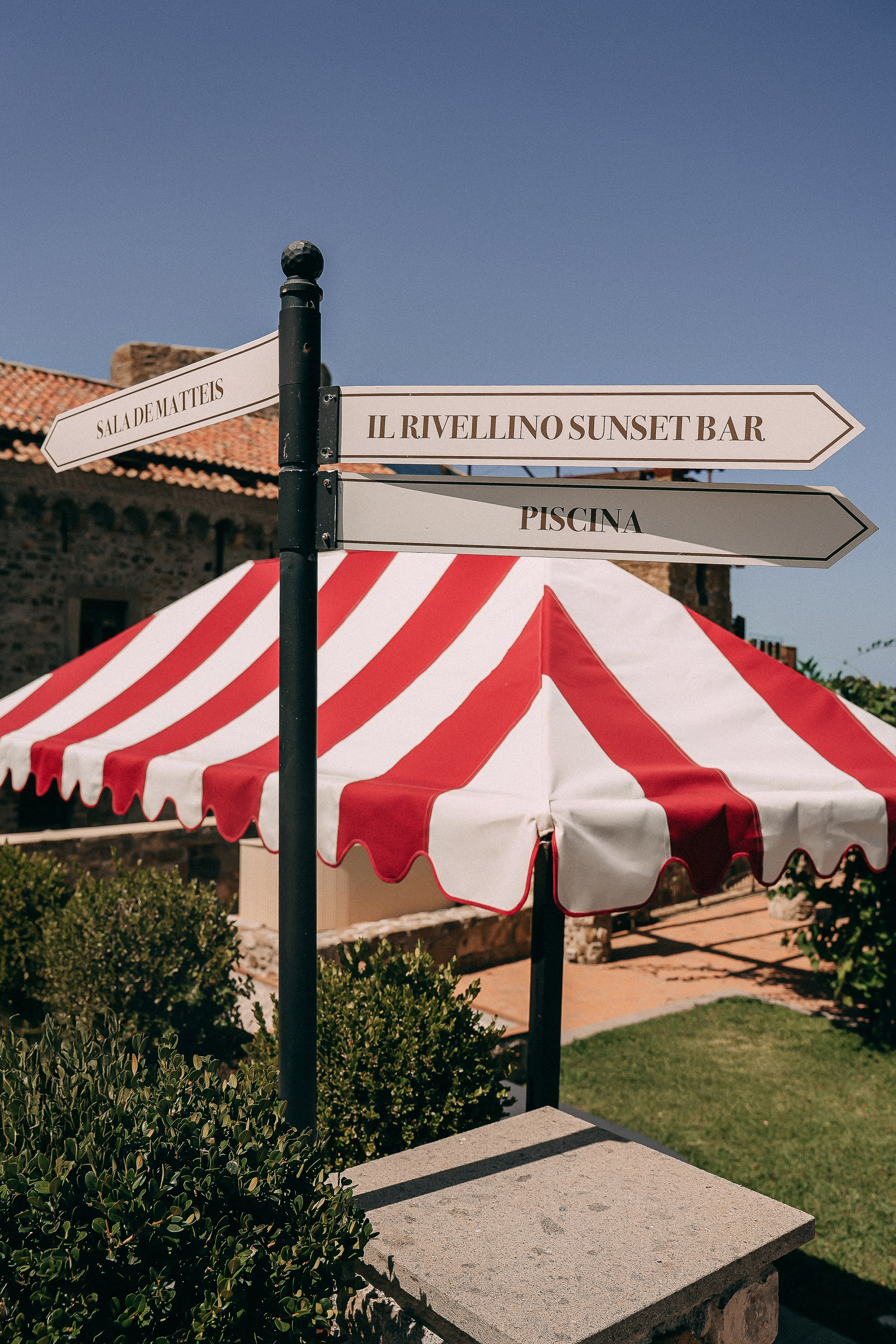 Vintage sign to Il Rivellino Sunset Bar and a red striped umbrella at the castle