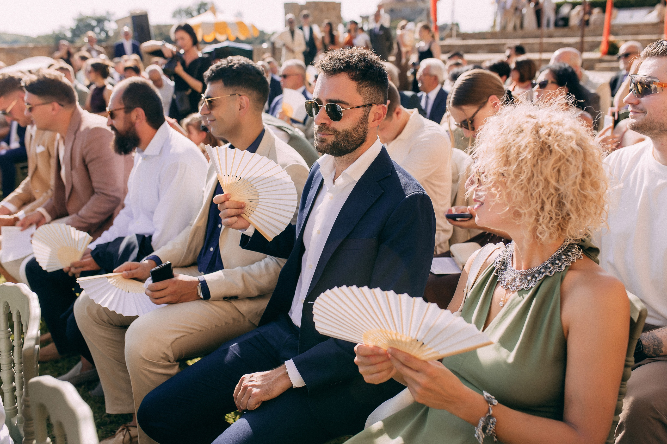 Wedding guests using fans in the summer heat during the ceremony