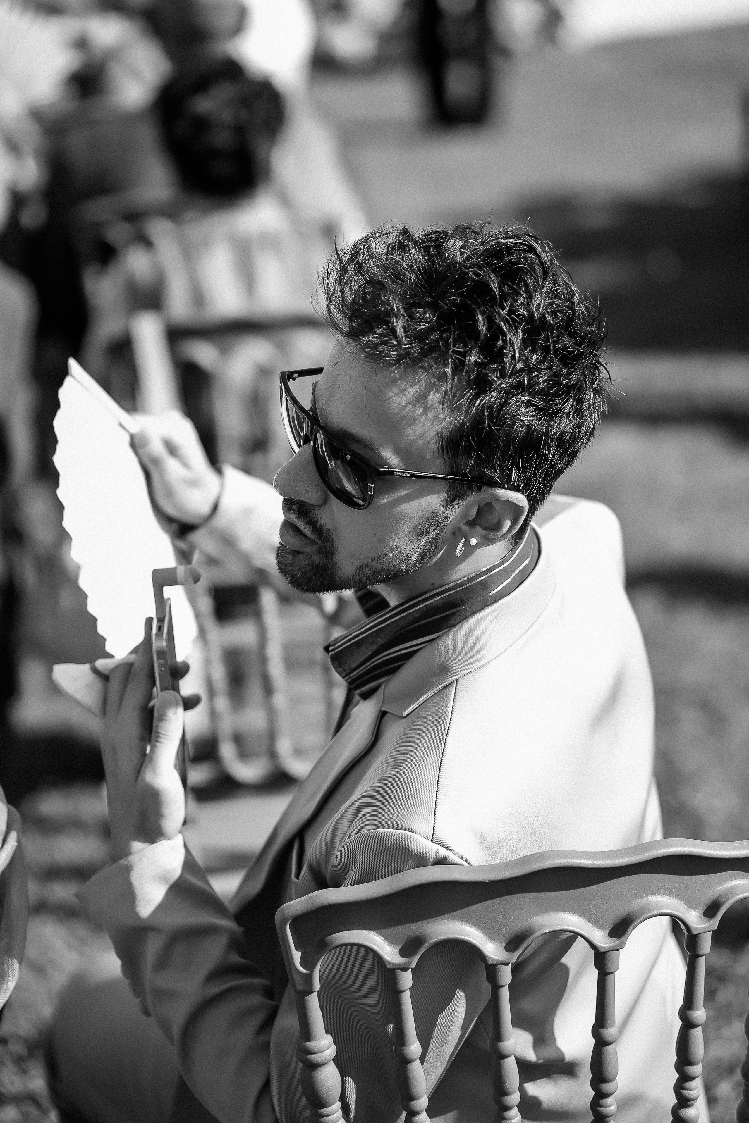 Black and white photo of a guest cooling off with a fan during the ceremony