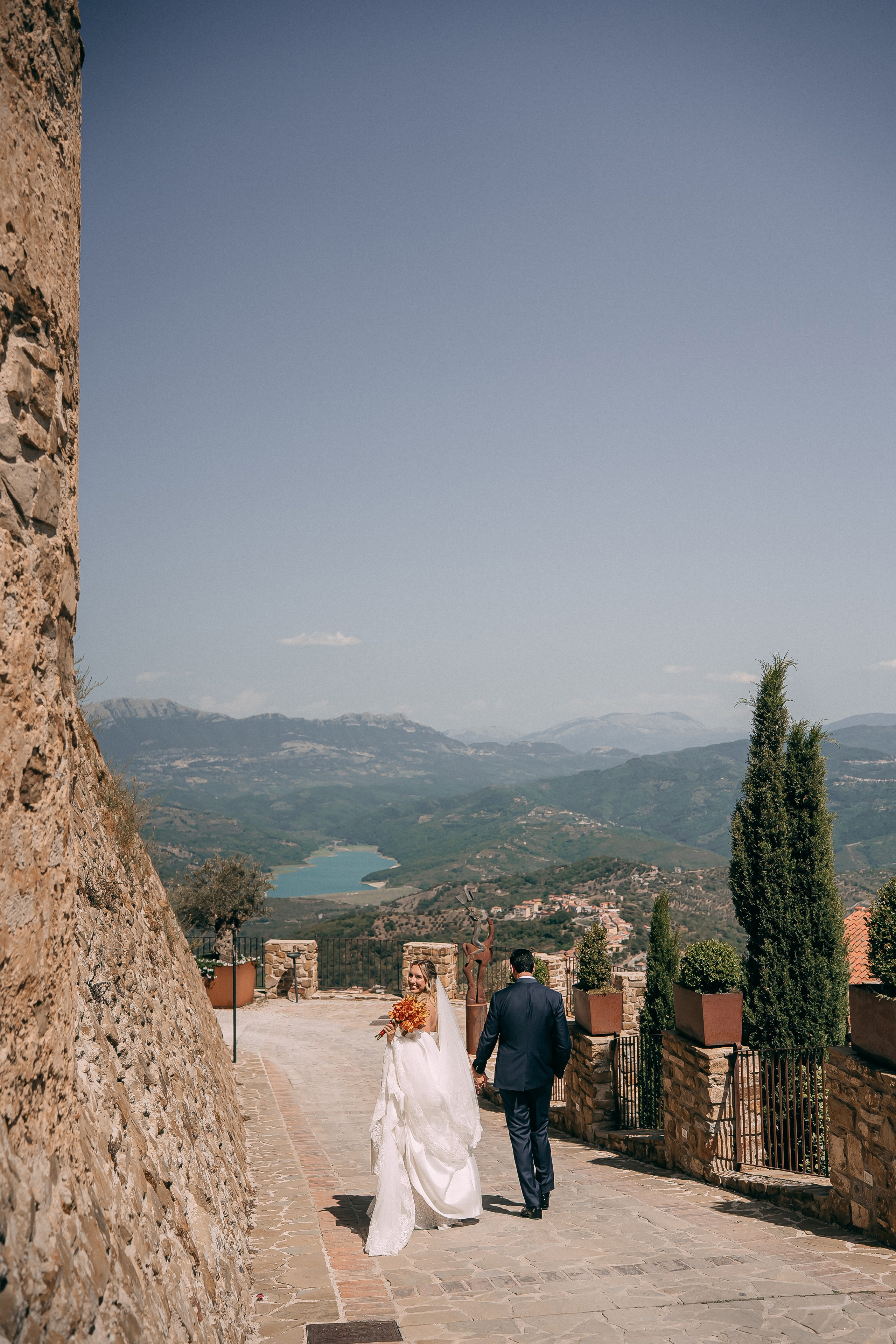 Bride and groom walking down the castle path with an orange bouquet