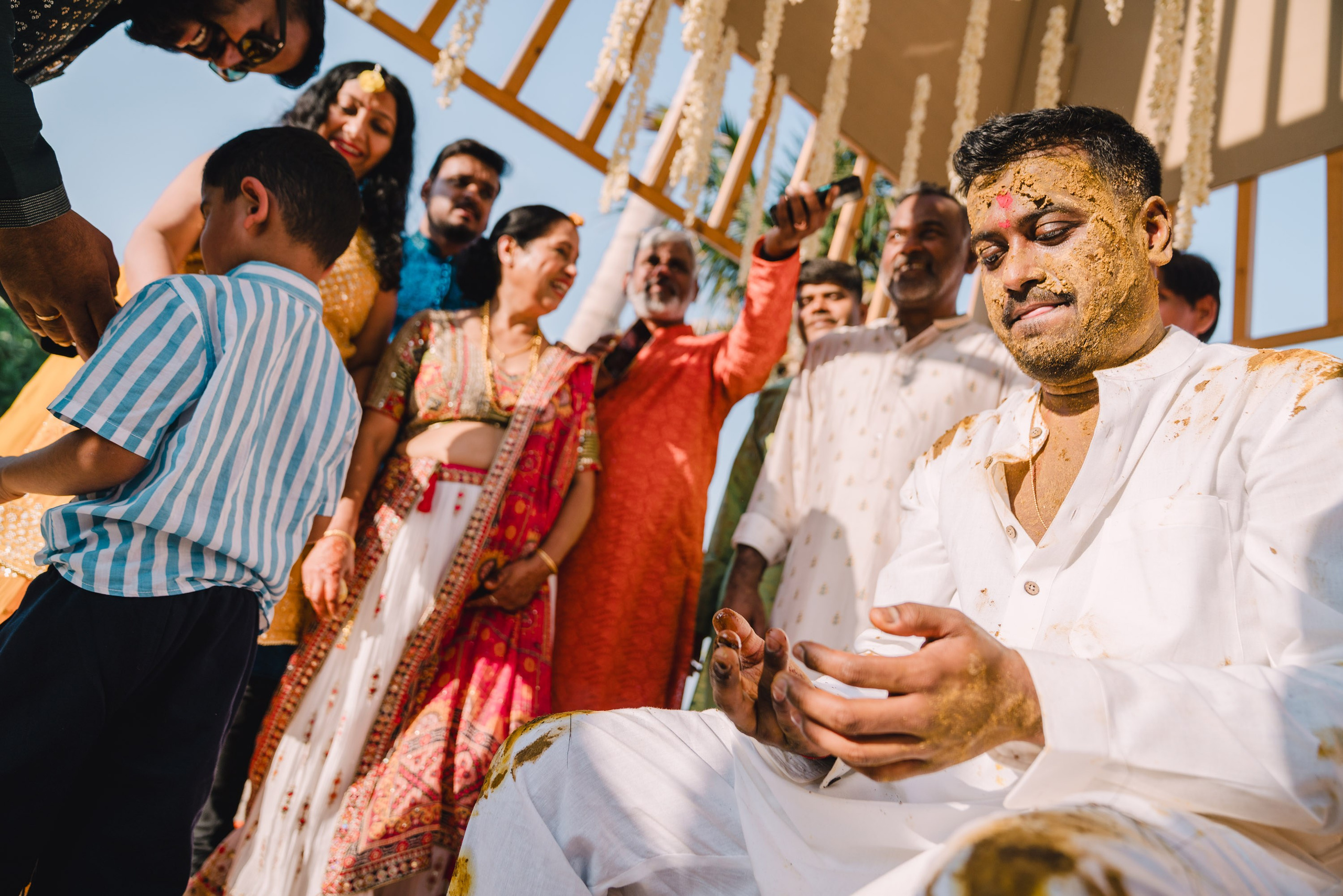 the groom with his face fully painted with turmeric is looking at his dirty hands with confusion