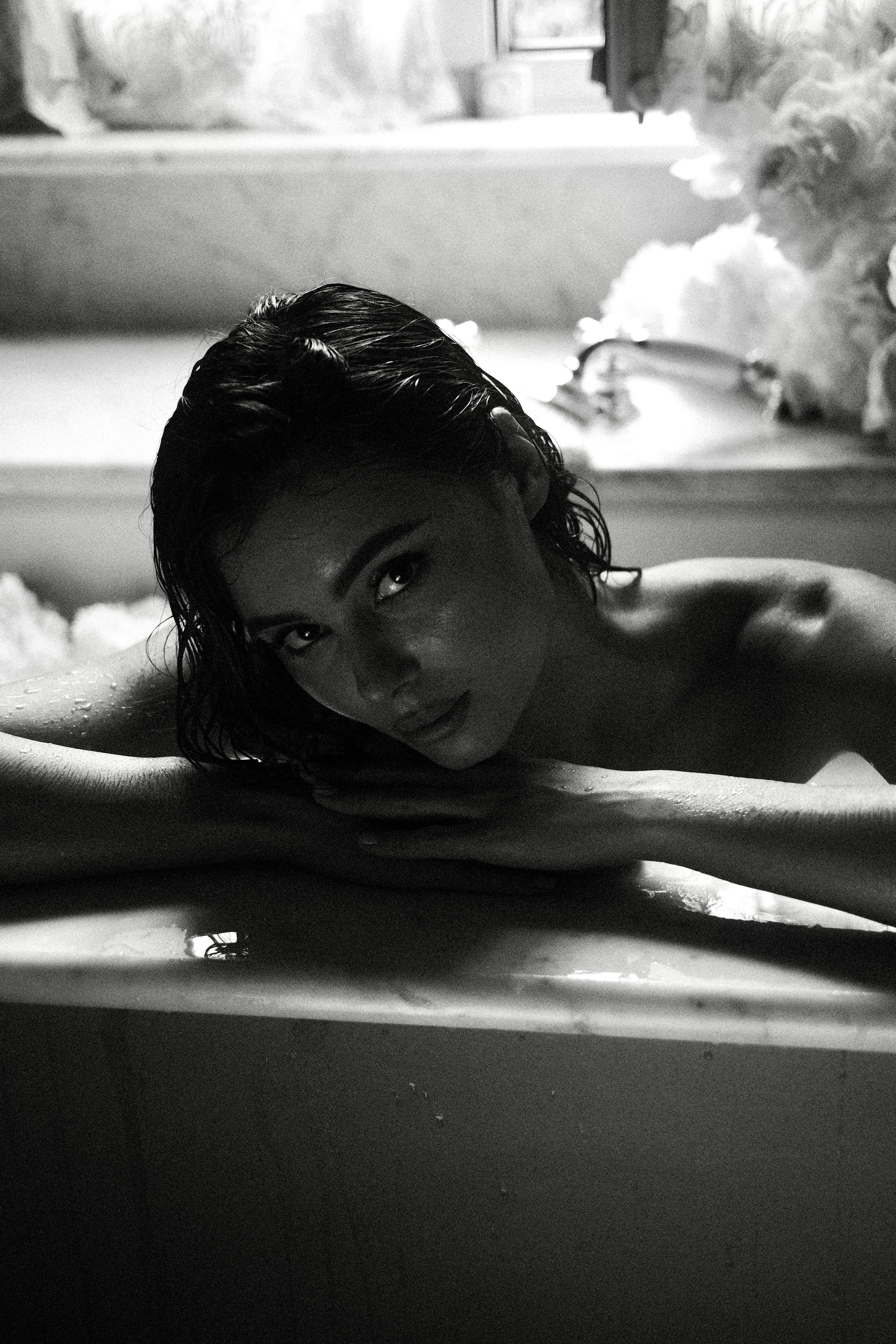 A dramatic black-and-white photo of a bride leaning over the edge of a bathtub, her face partially lit, with a mysterious ambiance.