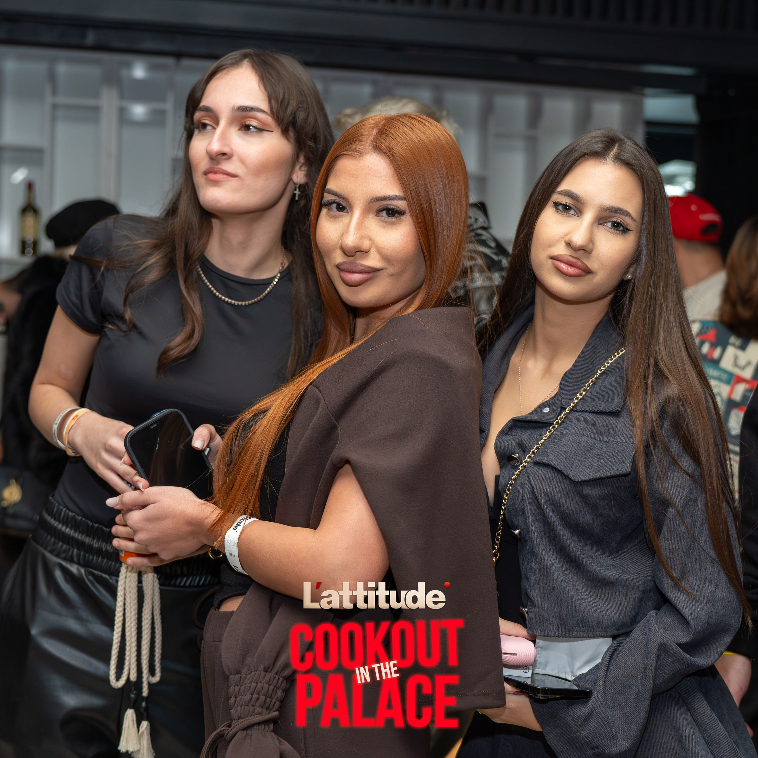 Three women standing closely together at an indoor event with casual outfits and neutral expressions.