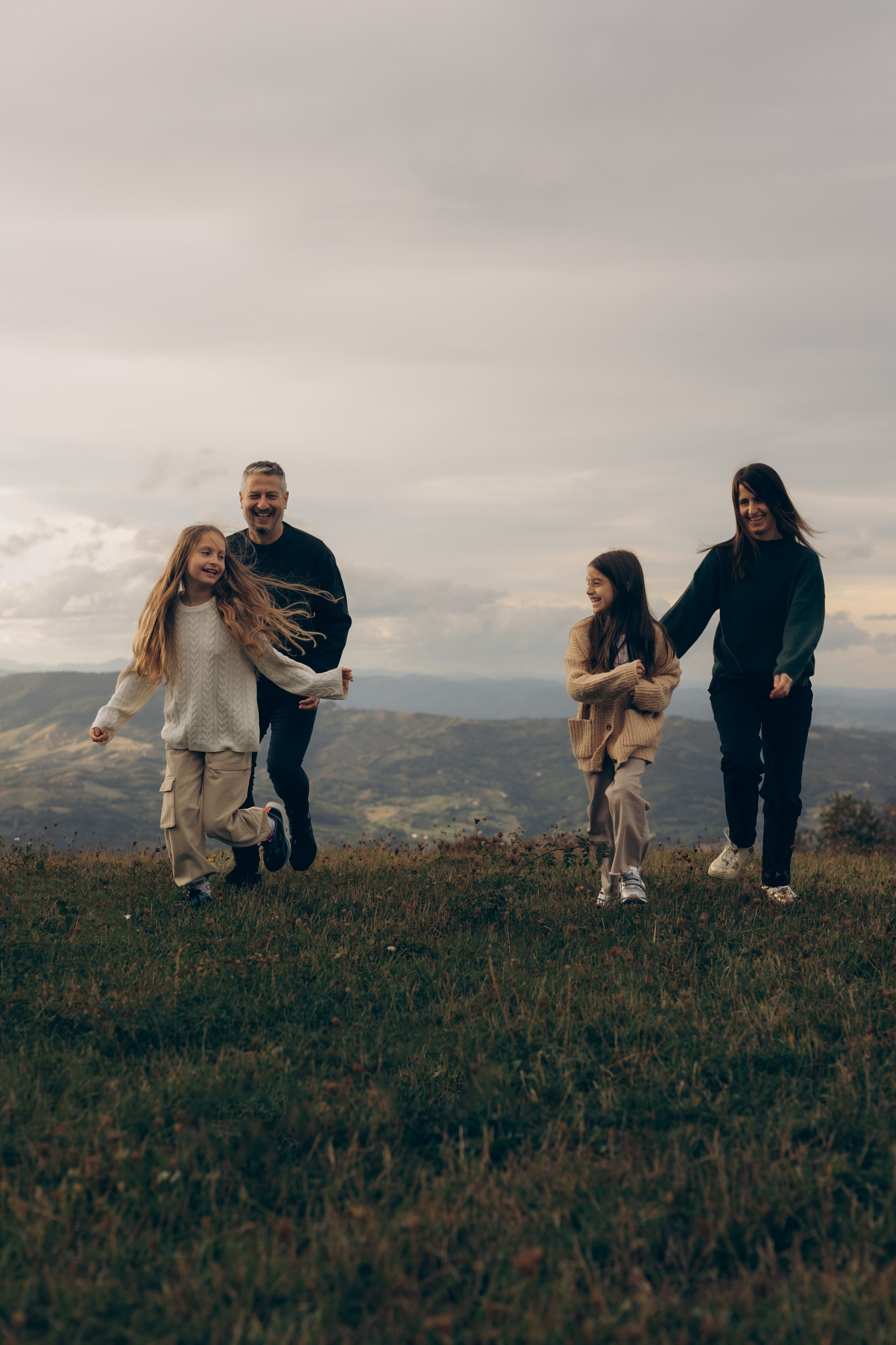 Famiglia con bambini che cammina lungo le montagne dell’Emilia-Romagna, risate, movimento e percorso condiviso nel paesaggio aperto.