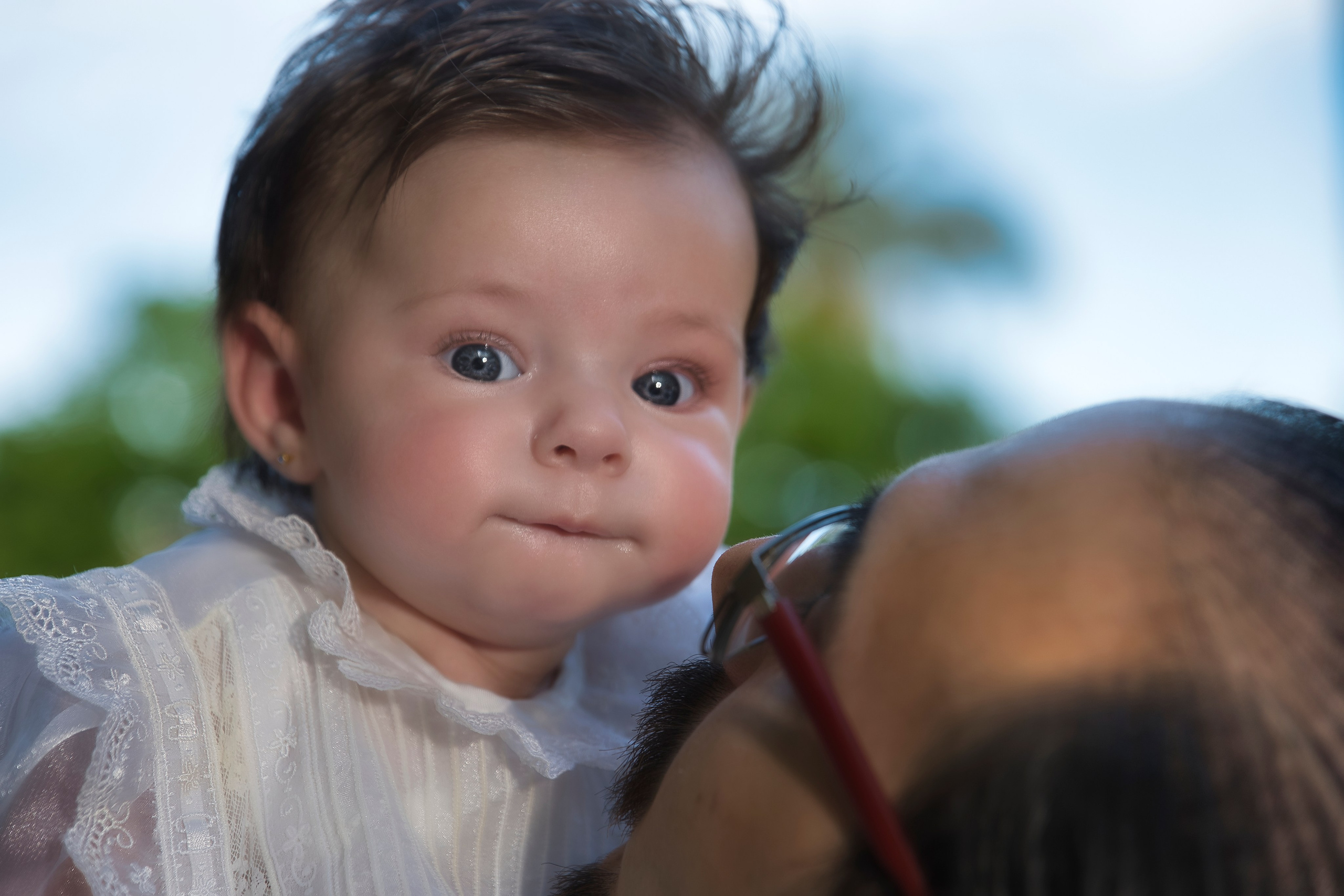 Niña vestida con traje de bautizo blanco, sostenida por sus padres en la iglesia.