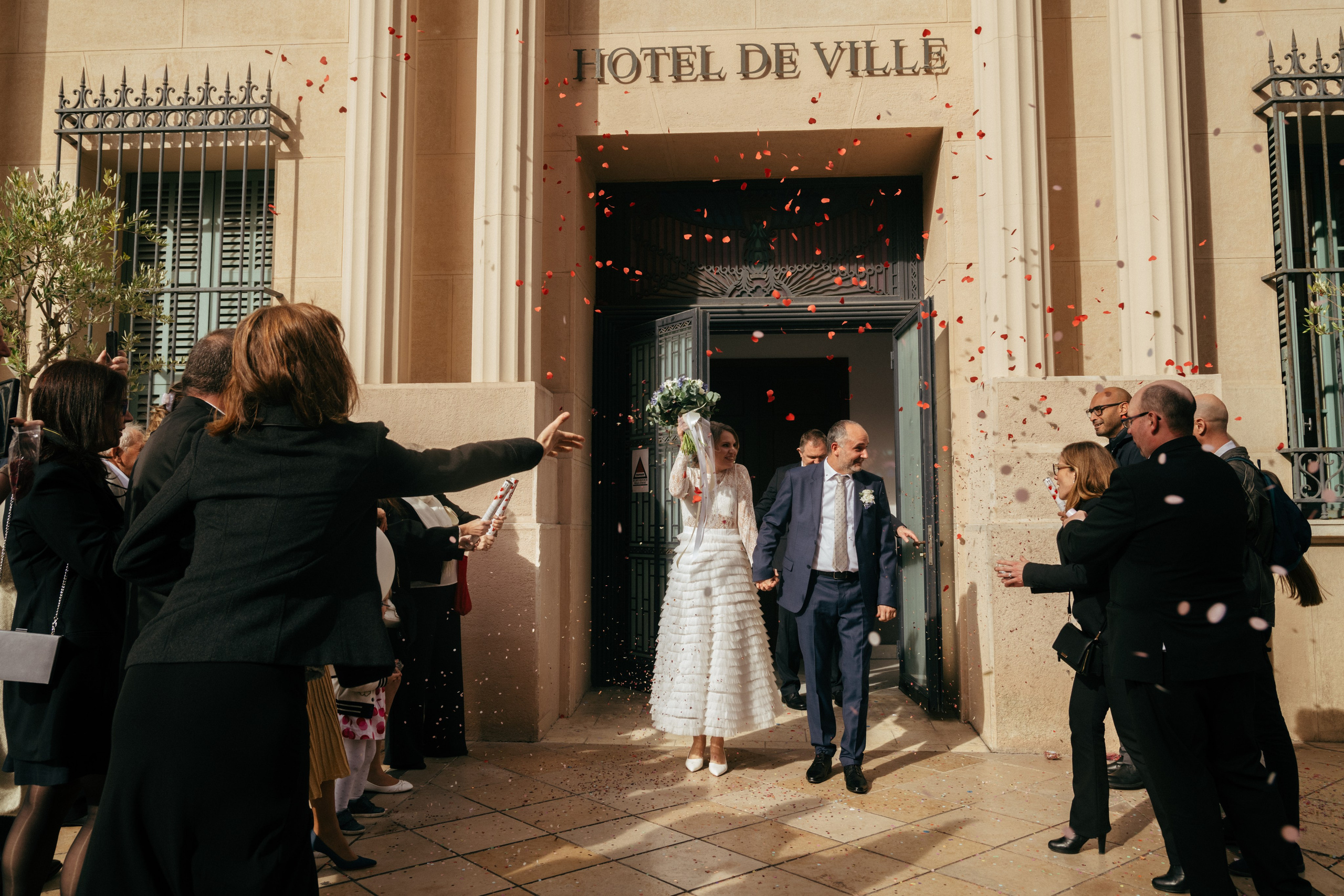 Les mariés sortent de la mairie pendant que les invités jettent des confettis.