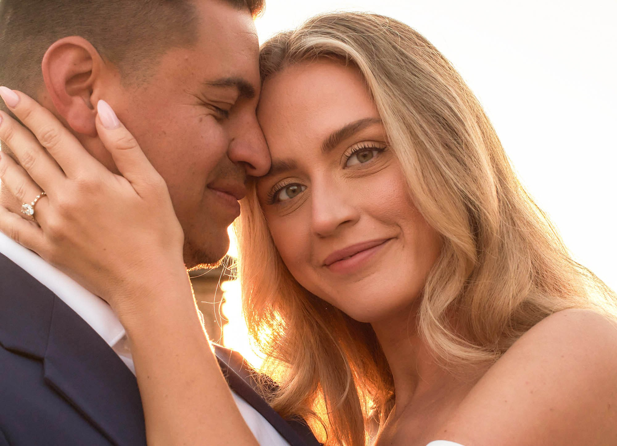 Blonde fiancée looking at camera while stroking fiancé's face during engagement session.