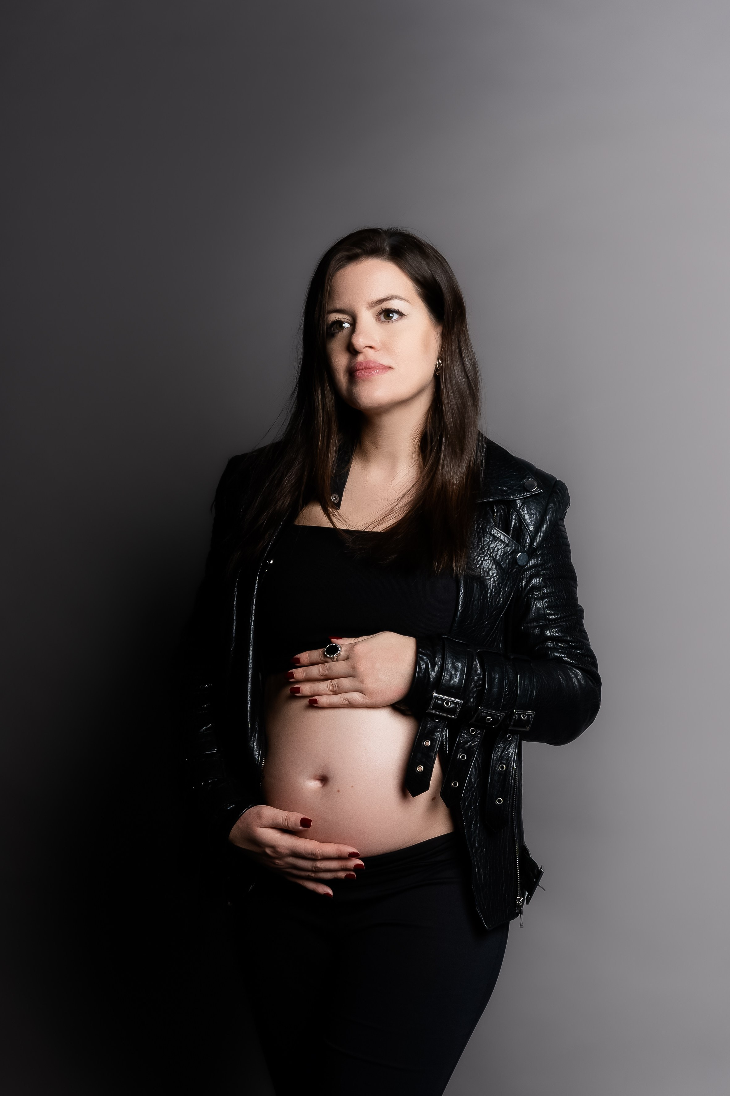 studijski portret trudnice koja zamišljeno gleda u daljinu sa rukama na stoma