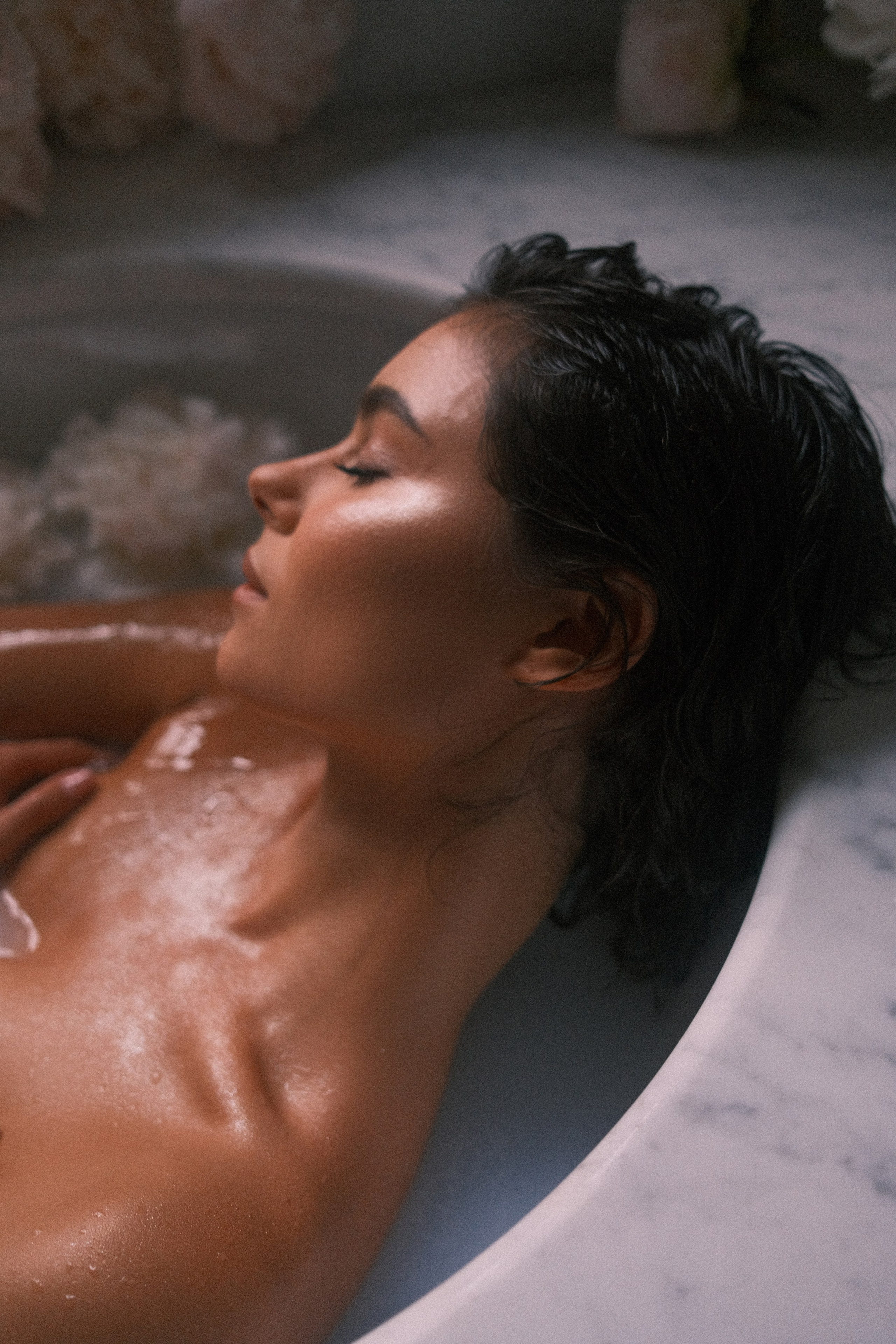 A profile view of a woman resting peacefully in a luxurious bath, her serene expression illuminated by soft, diffused light.