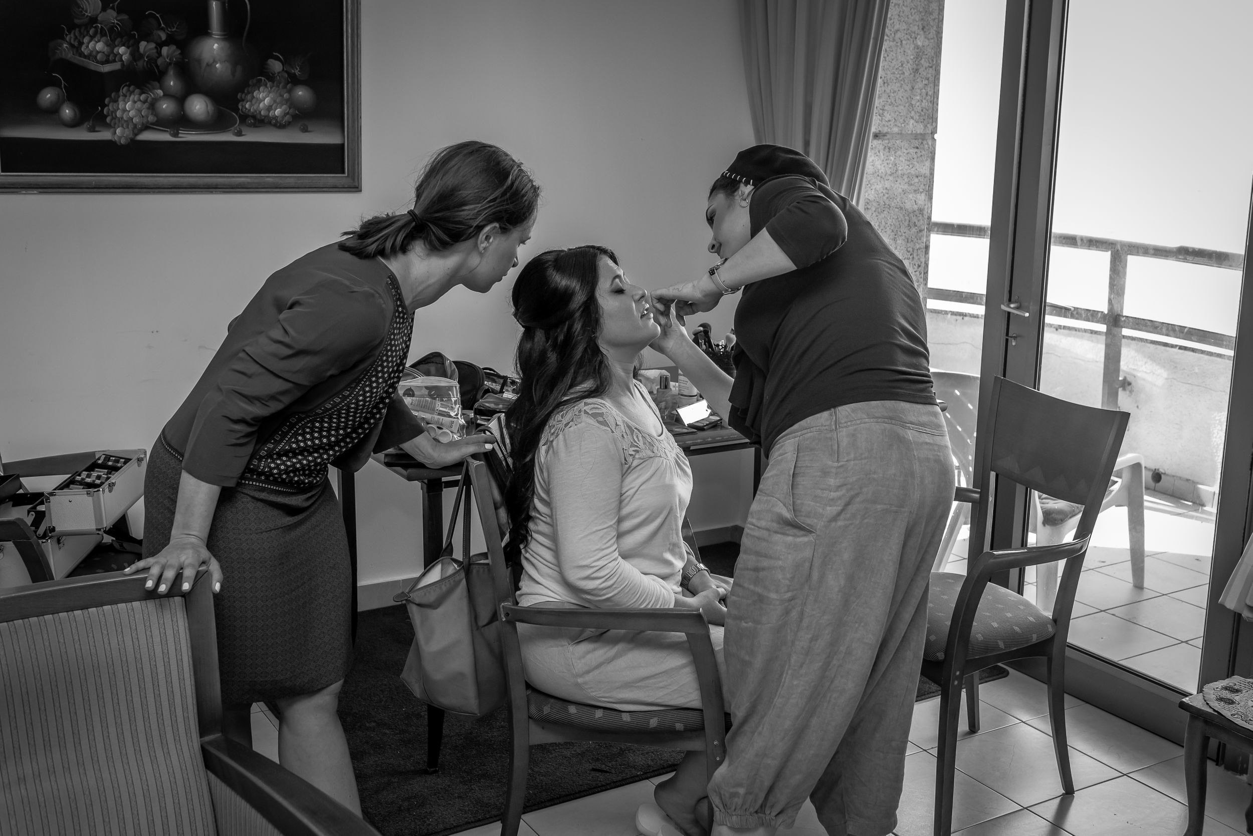 A makeup artist works on a bride as her friend watches