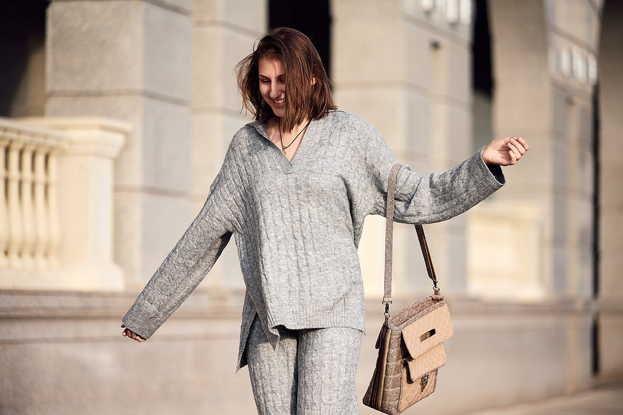 Портрет девушки в сером вязанном костюме и бежевой сумкой с распущенными каштановыми волосами