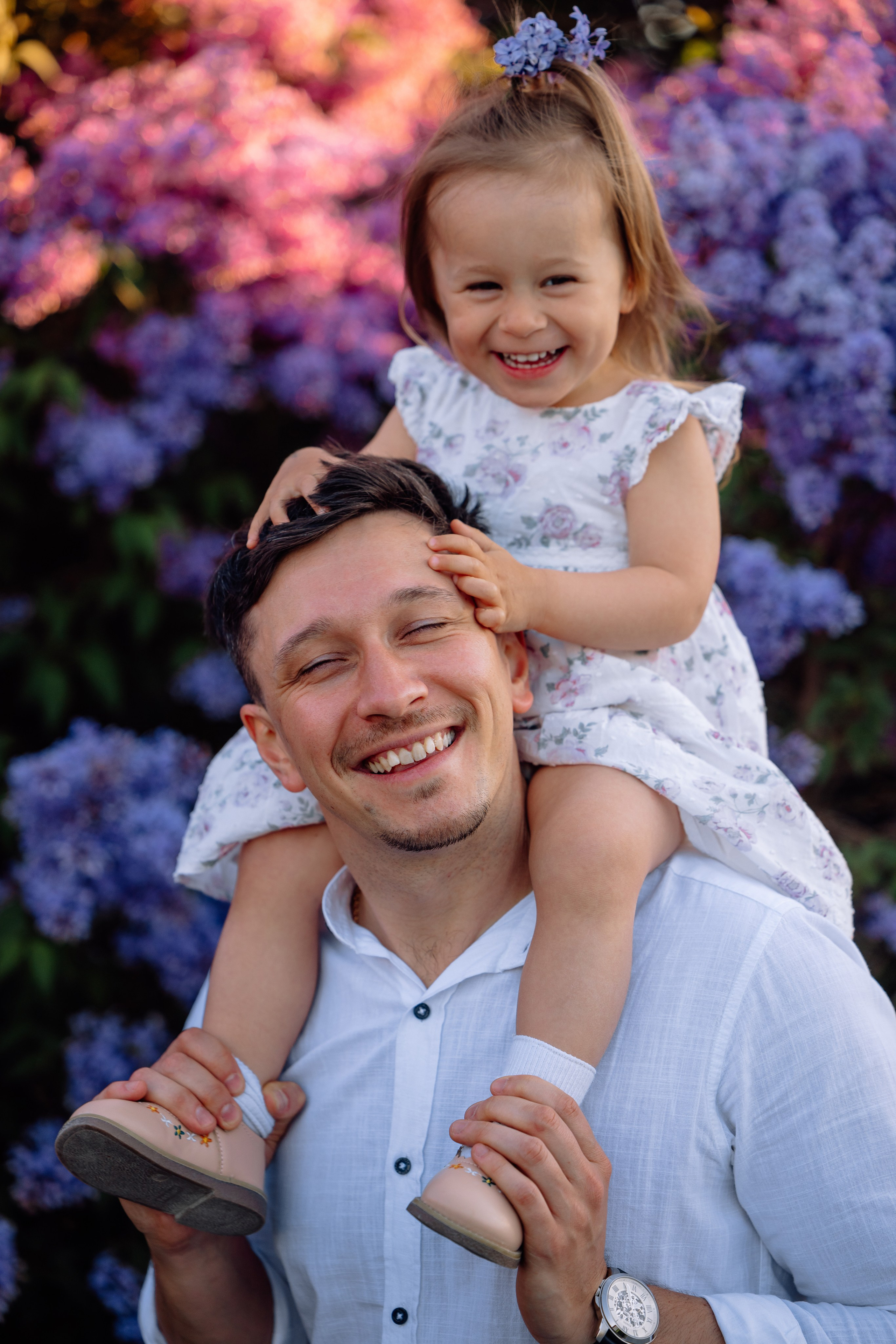 Tochter sitzt auf Papas Schultern und spielt mit seinen Haaren im Park vom Schloss Nymphenburg