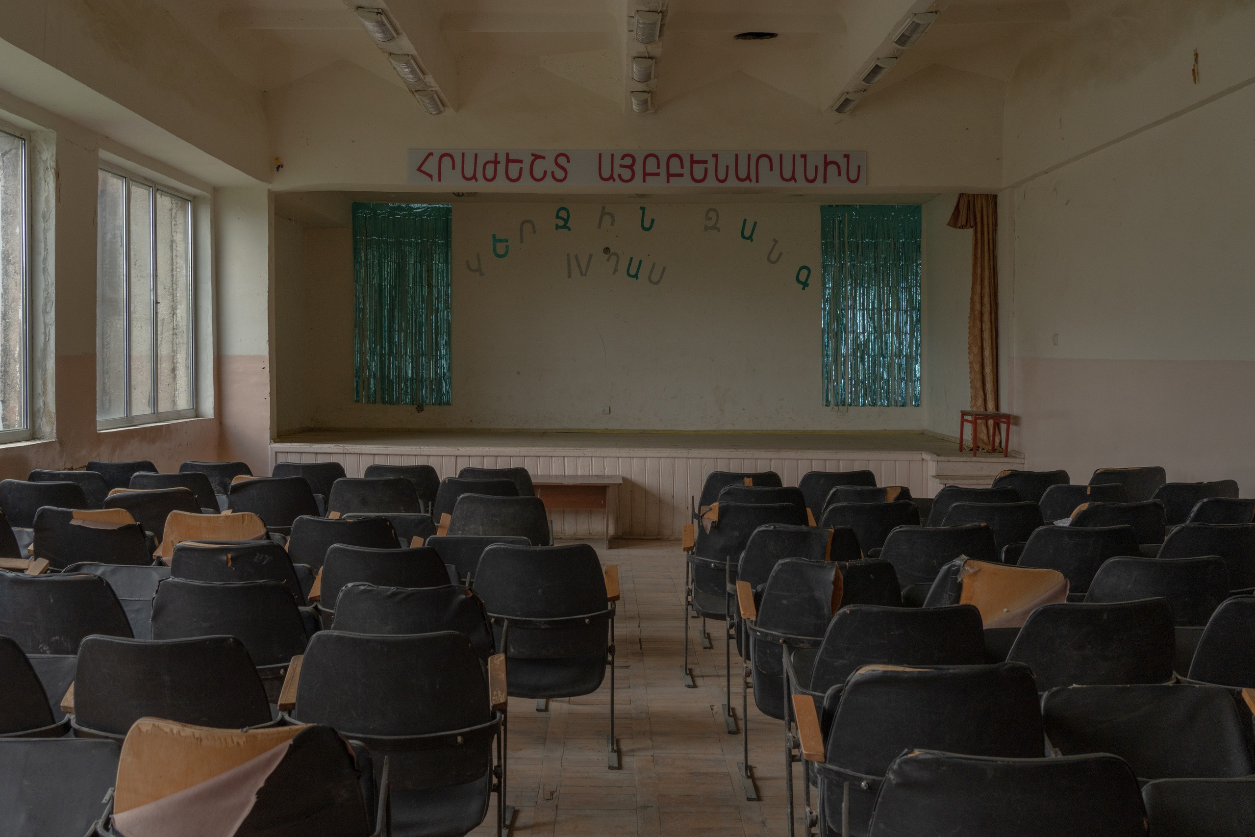 Aygedzor is a village in Tavush province, located on the border with Azerbaijan. A local school is building a cement wall to protect the children from potential cross-border shootings. Despite the threat and a lack of resources in border areas, teachers and school administration in Aygedzor engage children in many artistic performances. Here, a concert hall in Aygedzor school is pictured. The sign on the stage says, Farewell to the ABCs. The Last Bell.