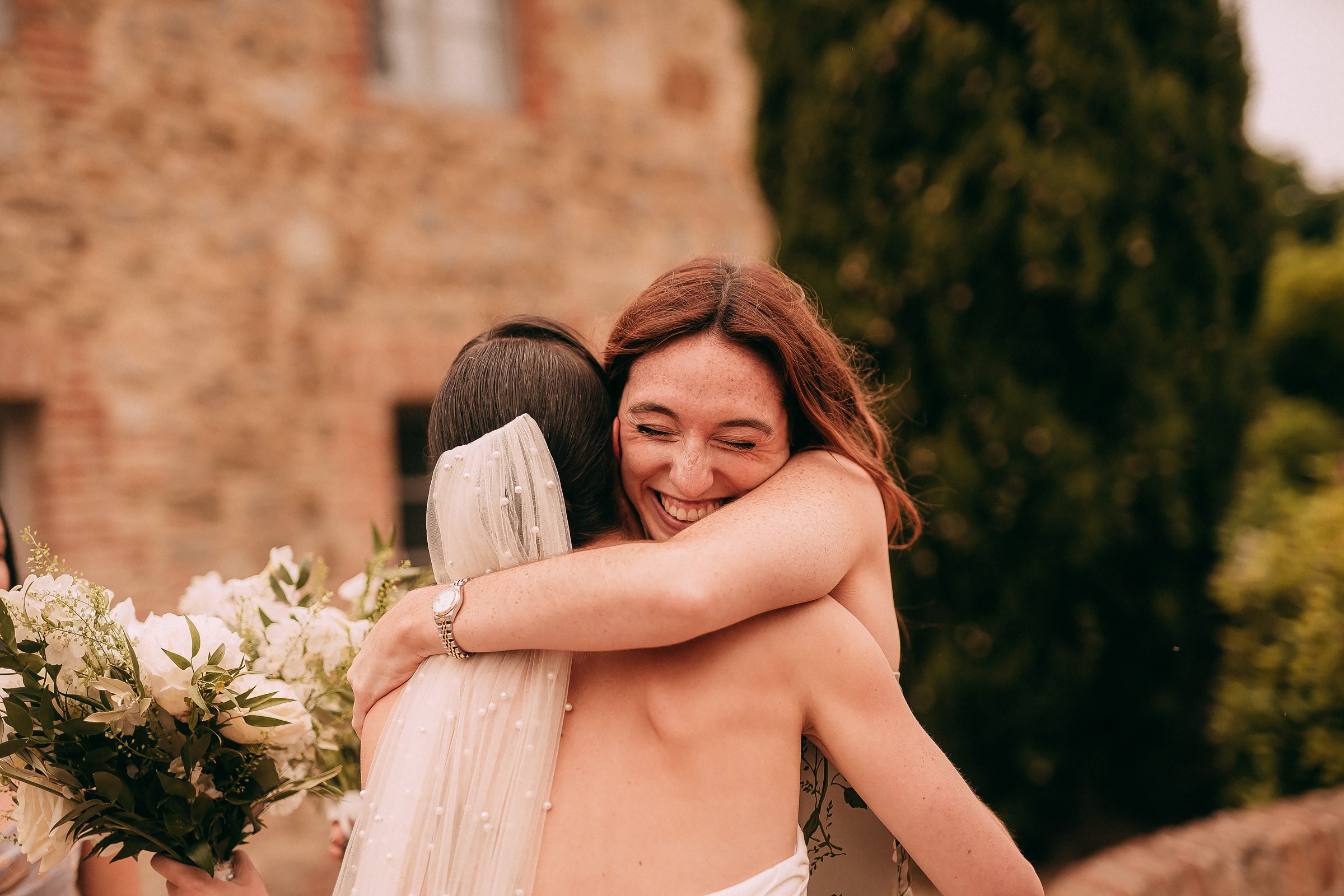 A heartfelt embrace between the bride and her bridesmaid, smiles radiating joy and love.