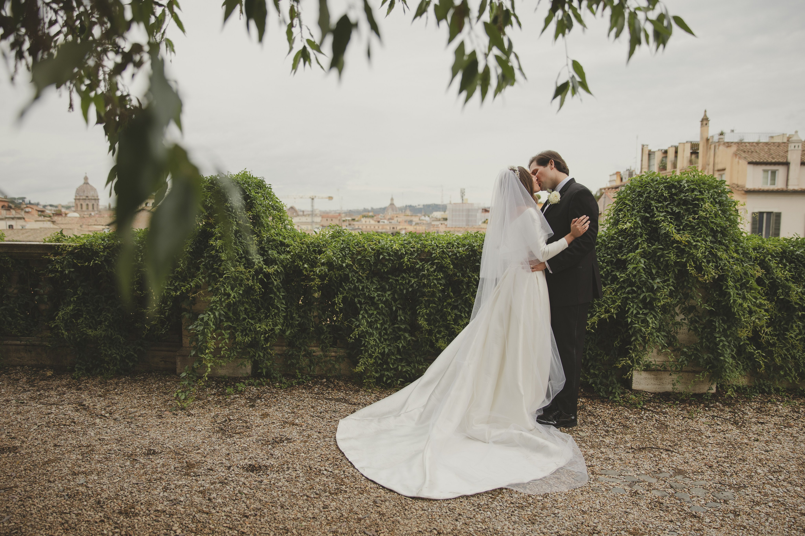 Newly married couple hugging in a luxury garden with sweeping views of Rome.