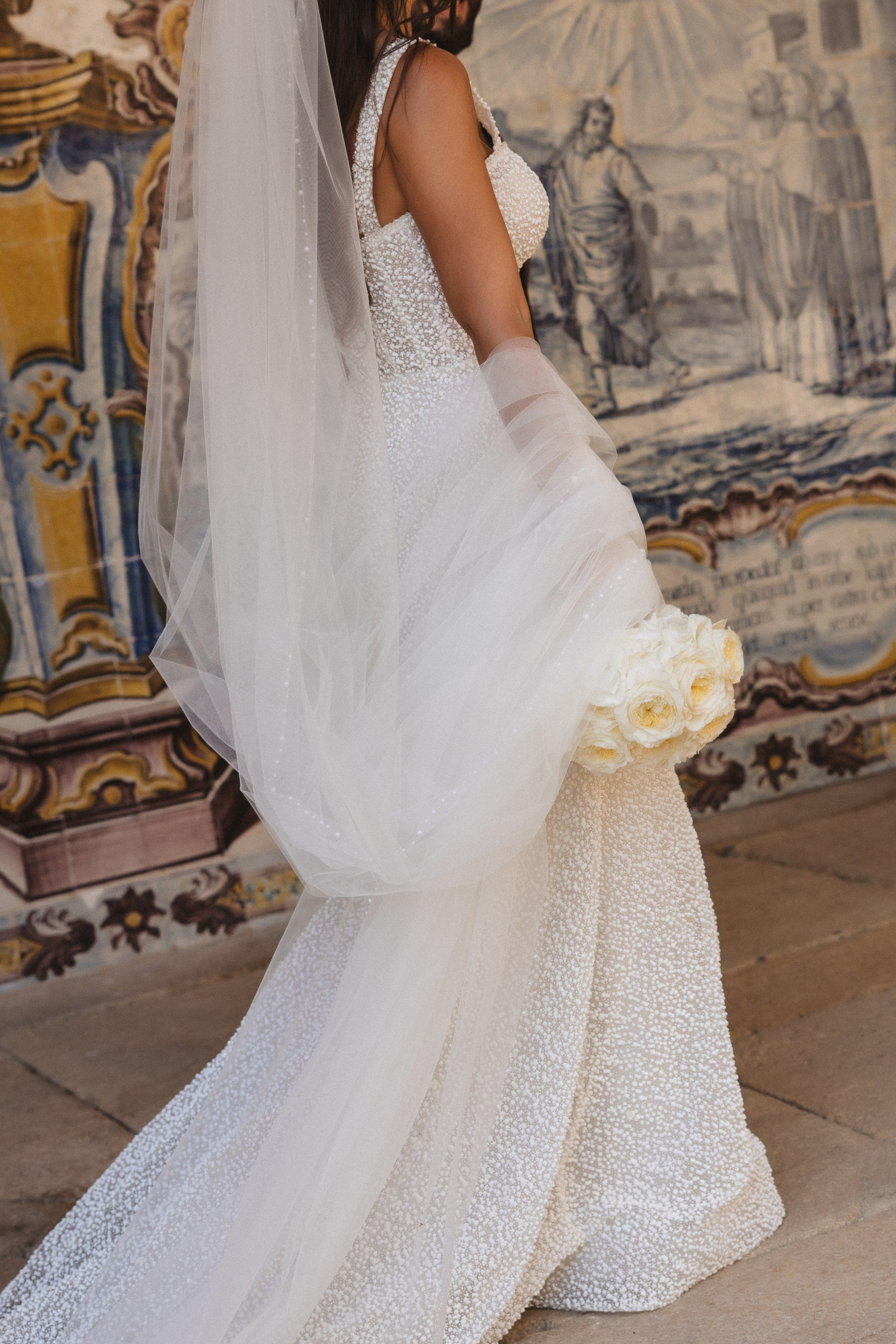 Noiva caminha ao lado de mural de azulejos típicos, num momento de elegância em casamento no Porto.