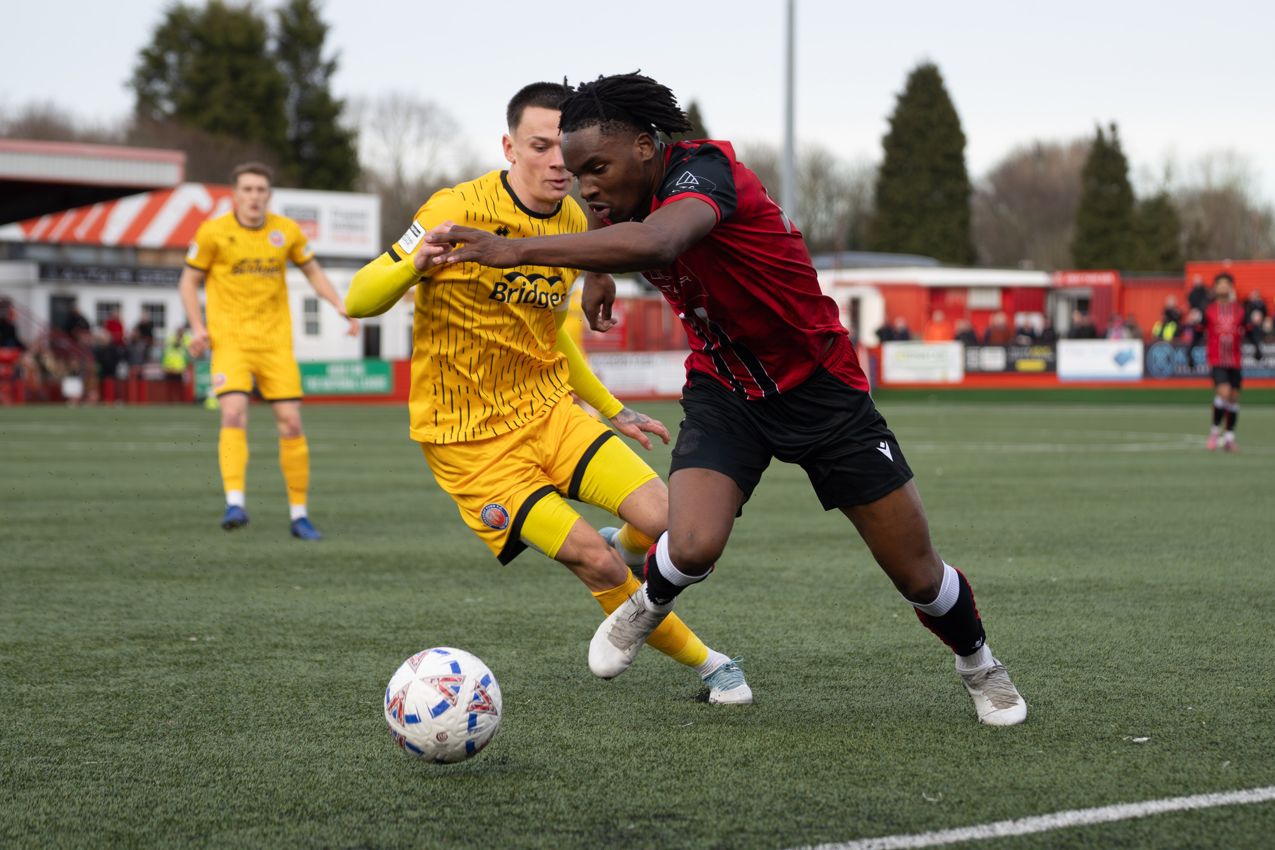Tamworth, England — February 14, 2026: Tamworth’s Daniel Isichei (red) holds off an Aldershot Town defender as he drives forward during the Enterprise National League match between Tamworth and Aldershot Town at The Lamb Ground. Photo: Jay Soundo
