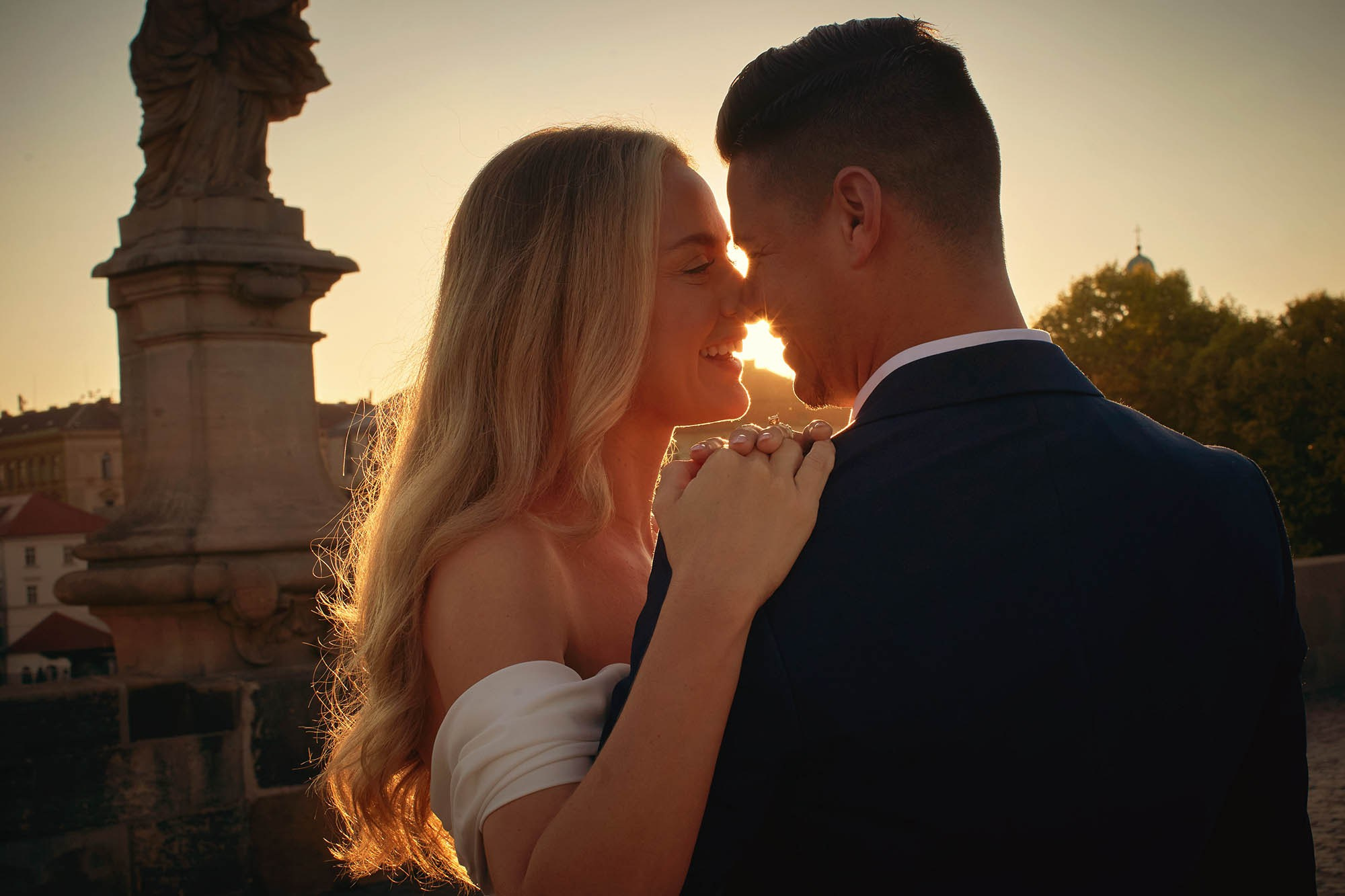 Tender embrace amid brilliant morning light on Prague's Charles Bridge.