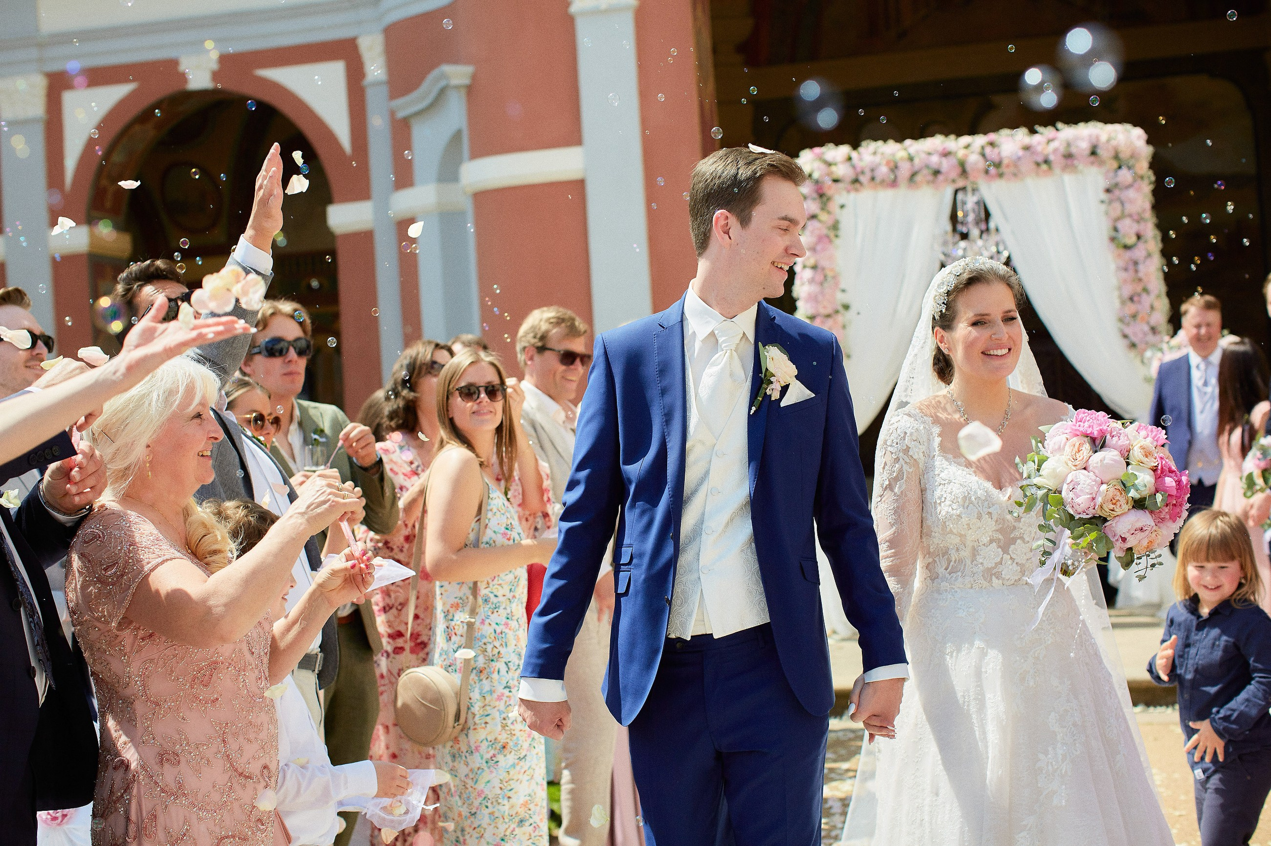 The smiling groom looks to his bride as bubles are blown and rose petals are tossed in their honor after their wedding ceremony at the Ledebour Garden.
