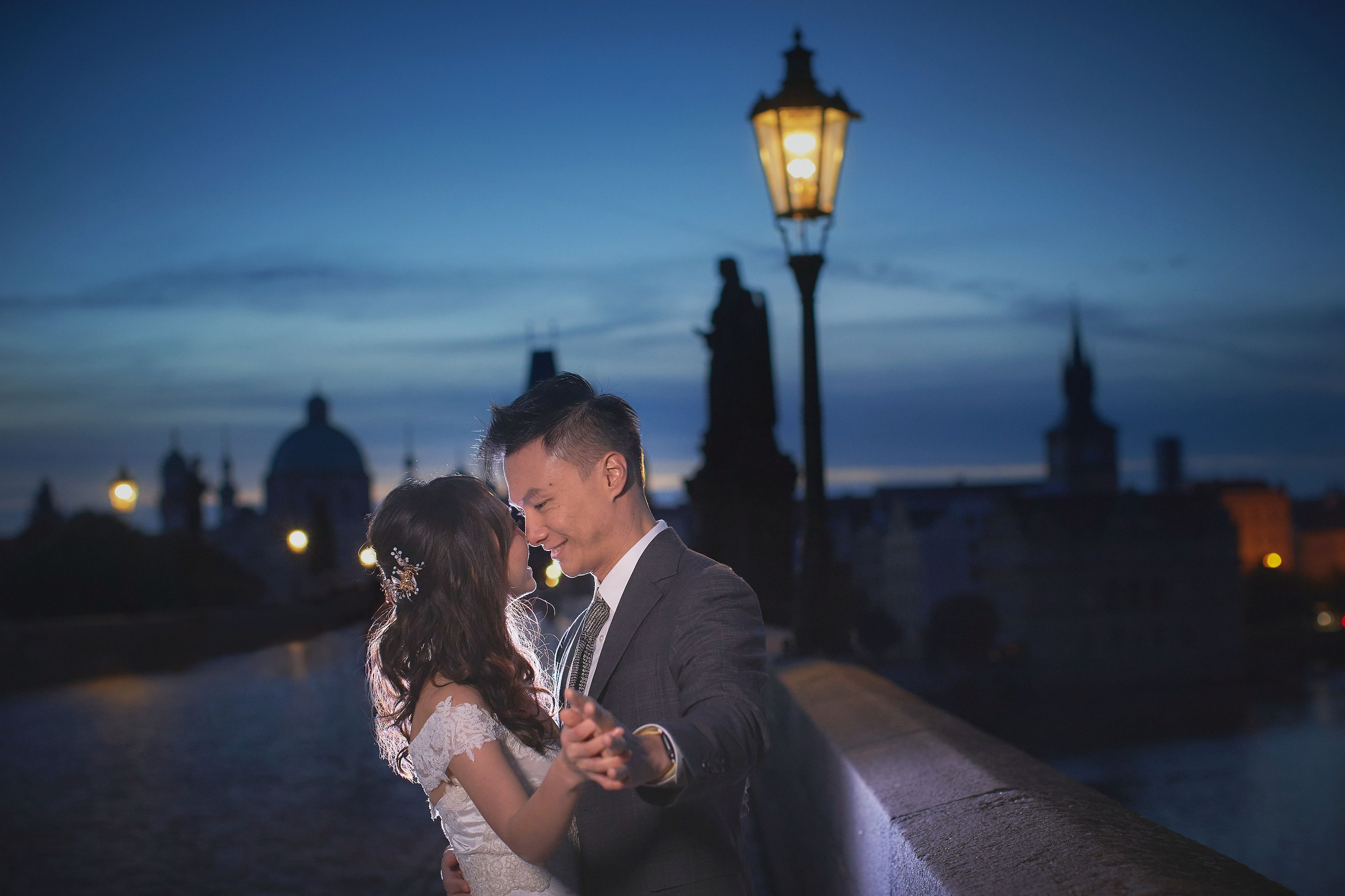 Eva and Conan are holding hands and embracing happily under gas lamps on Charles Bridge.
