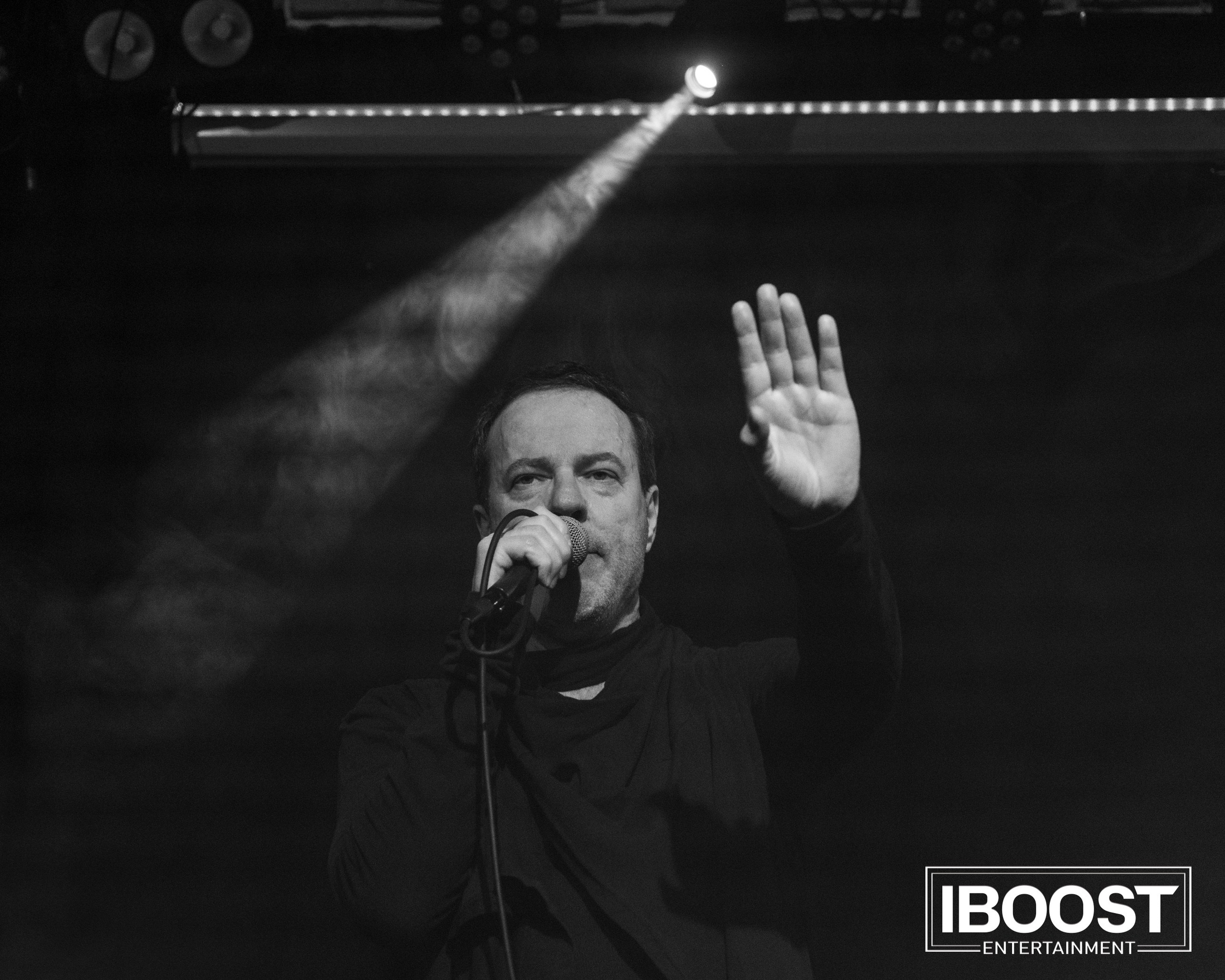 Black-and-white close-up of the lead vocalist of Animal JazZ singing on stage with one hand raised.