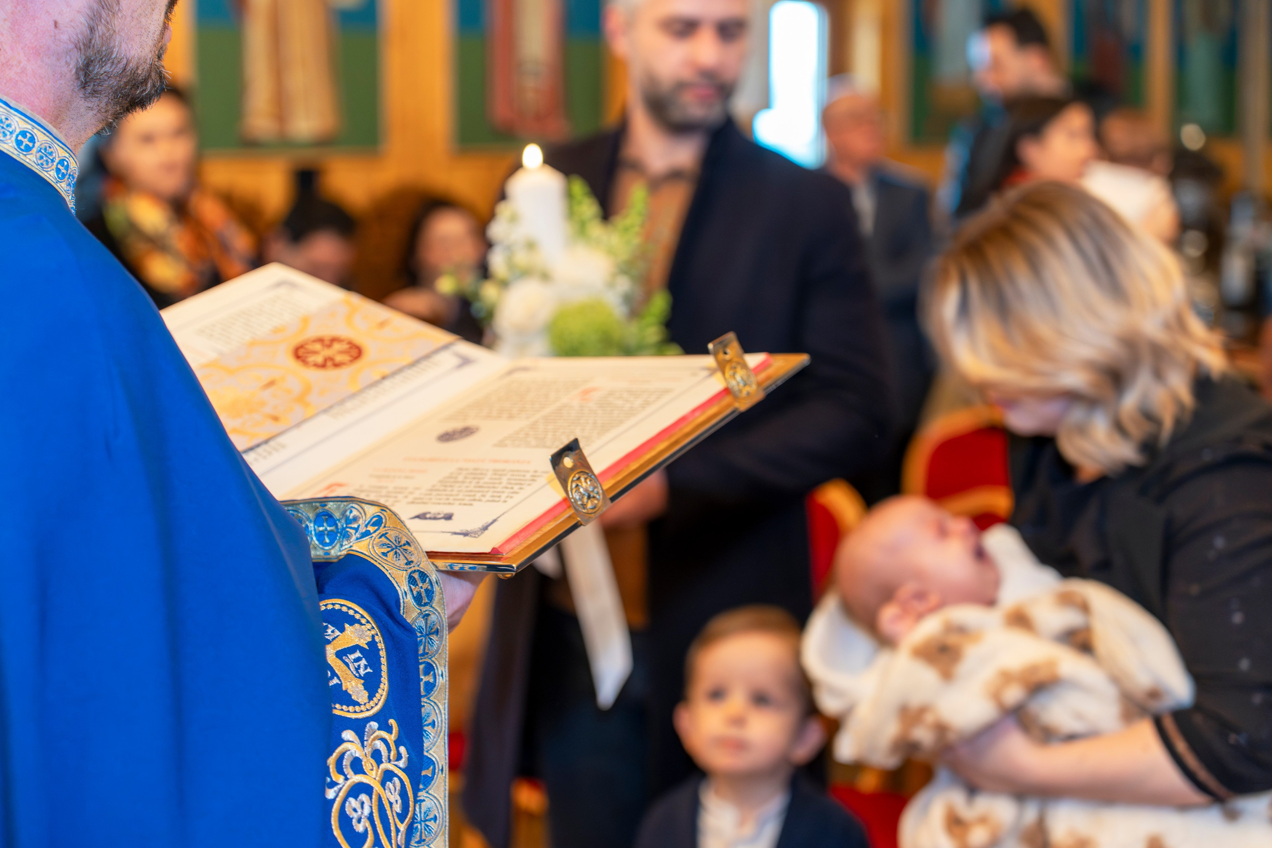 Priest reading from a book during a church baptism with family and crying baby.