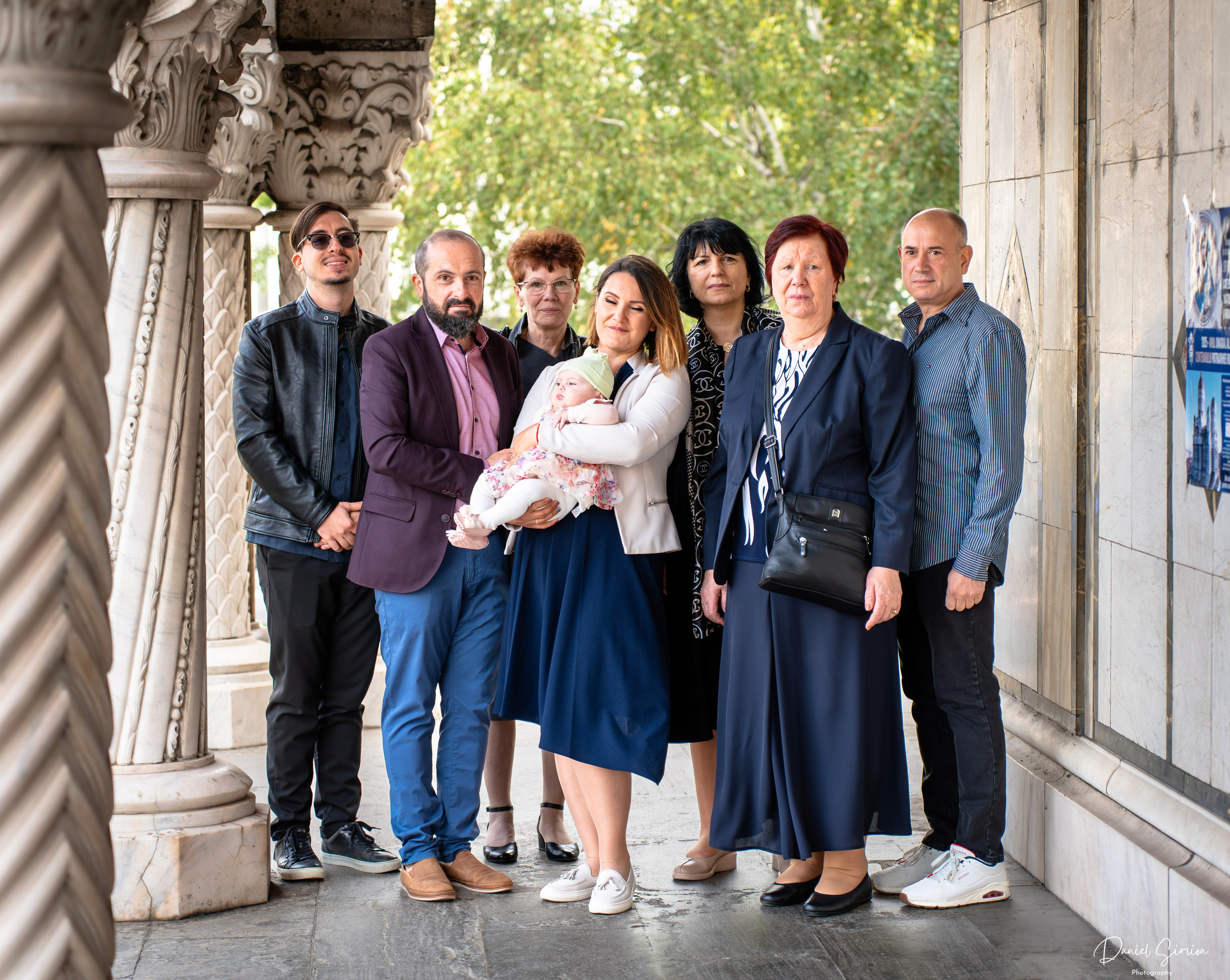 Group of seven adults with a baby, standing near carved stone columns outside a building.