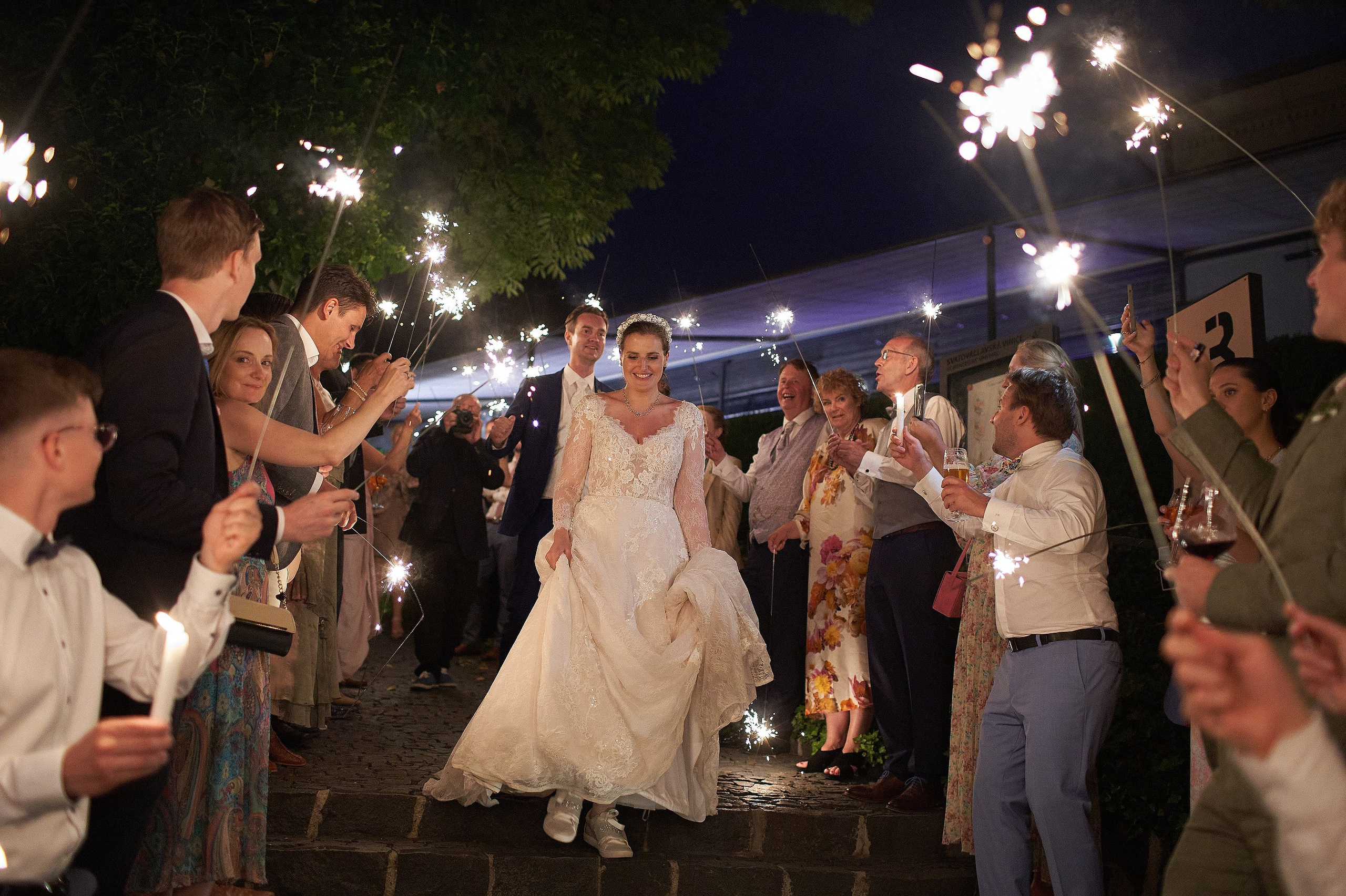 A bride and groom run though a crowd of well-wishers holding sparklers during an evening wedding reception at the Villa Richter in Prague.