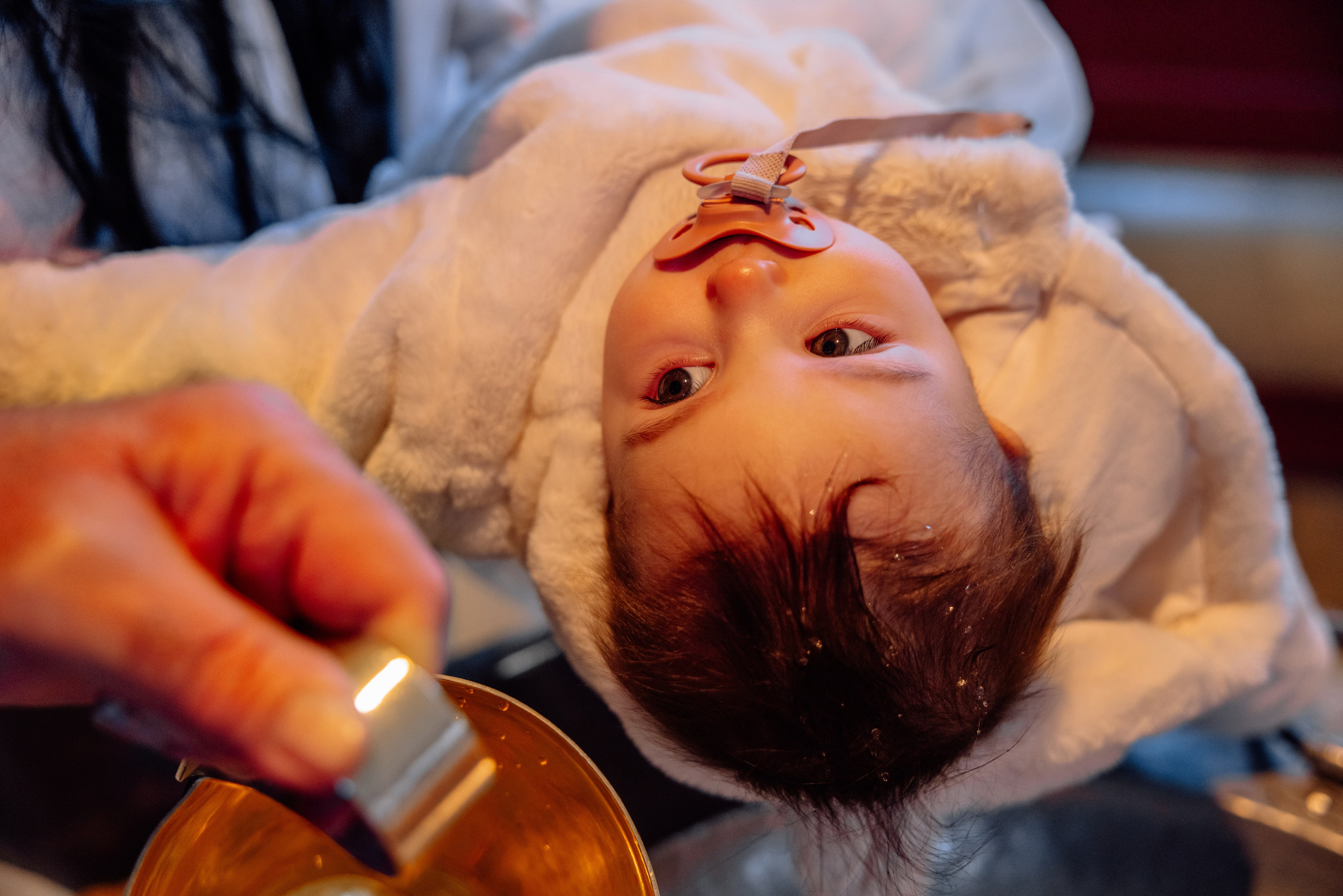 Priester gießt heiliges Wasser auf den Kopf des Babys – Taufe in Allach