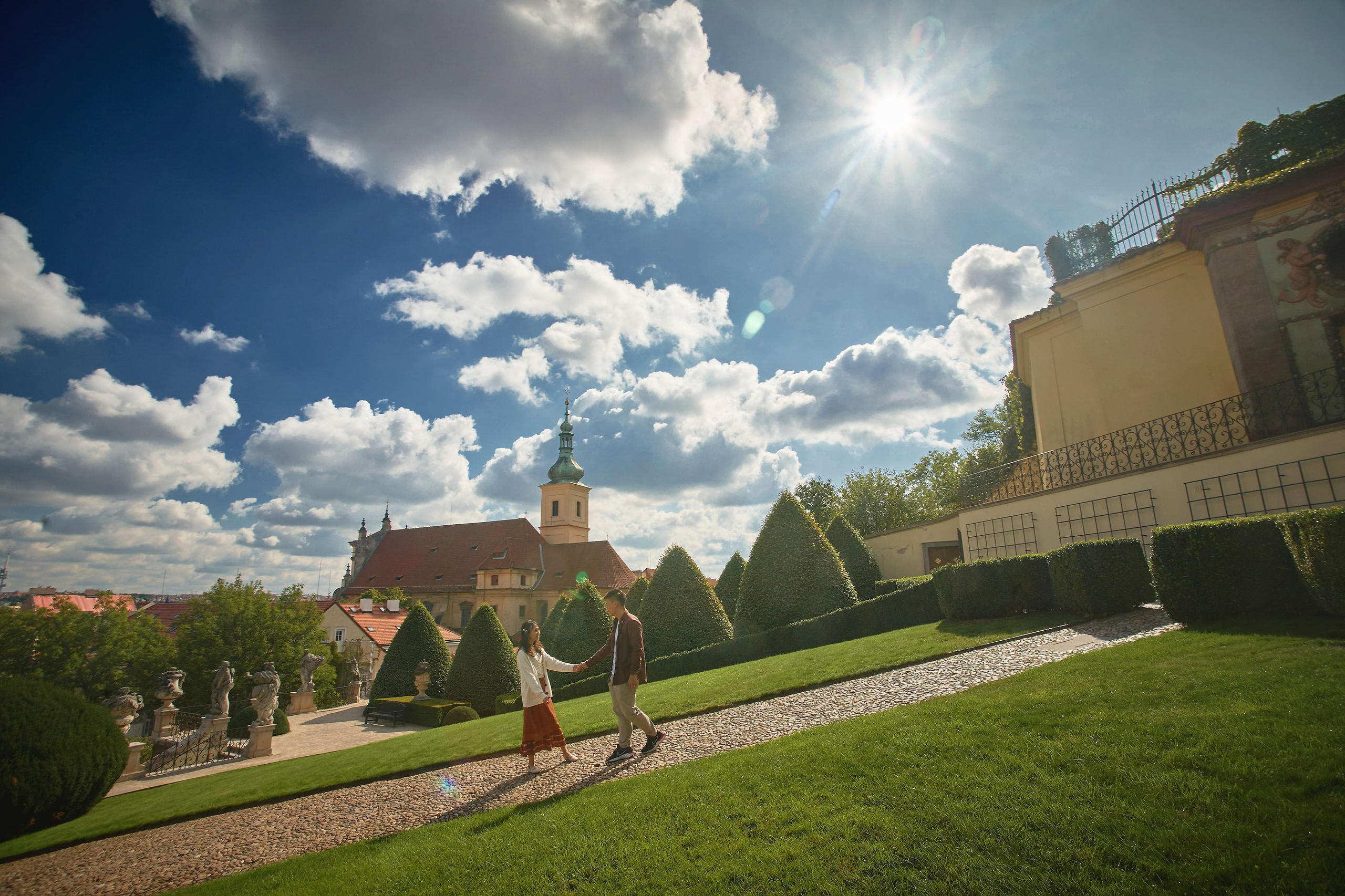 Wide-angle view of Eva and Conan walking down the path in Vrtba Garden with sun flare.