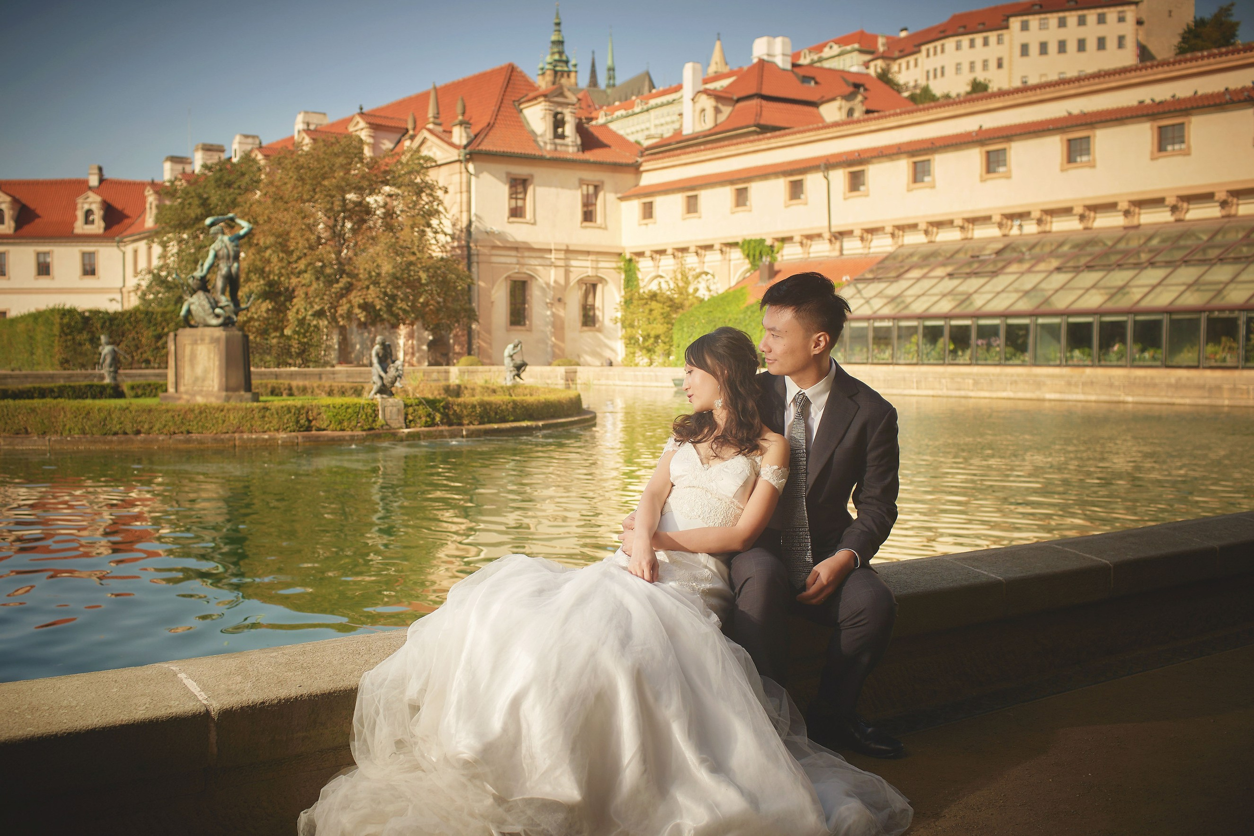 Newlyweds Eva and Conan by the pond in Wallenstein Garden with the Prague Castle skyline.