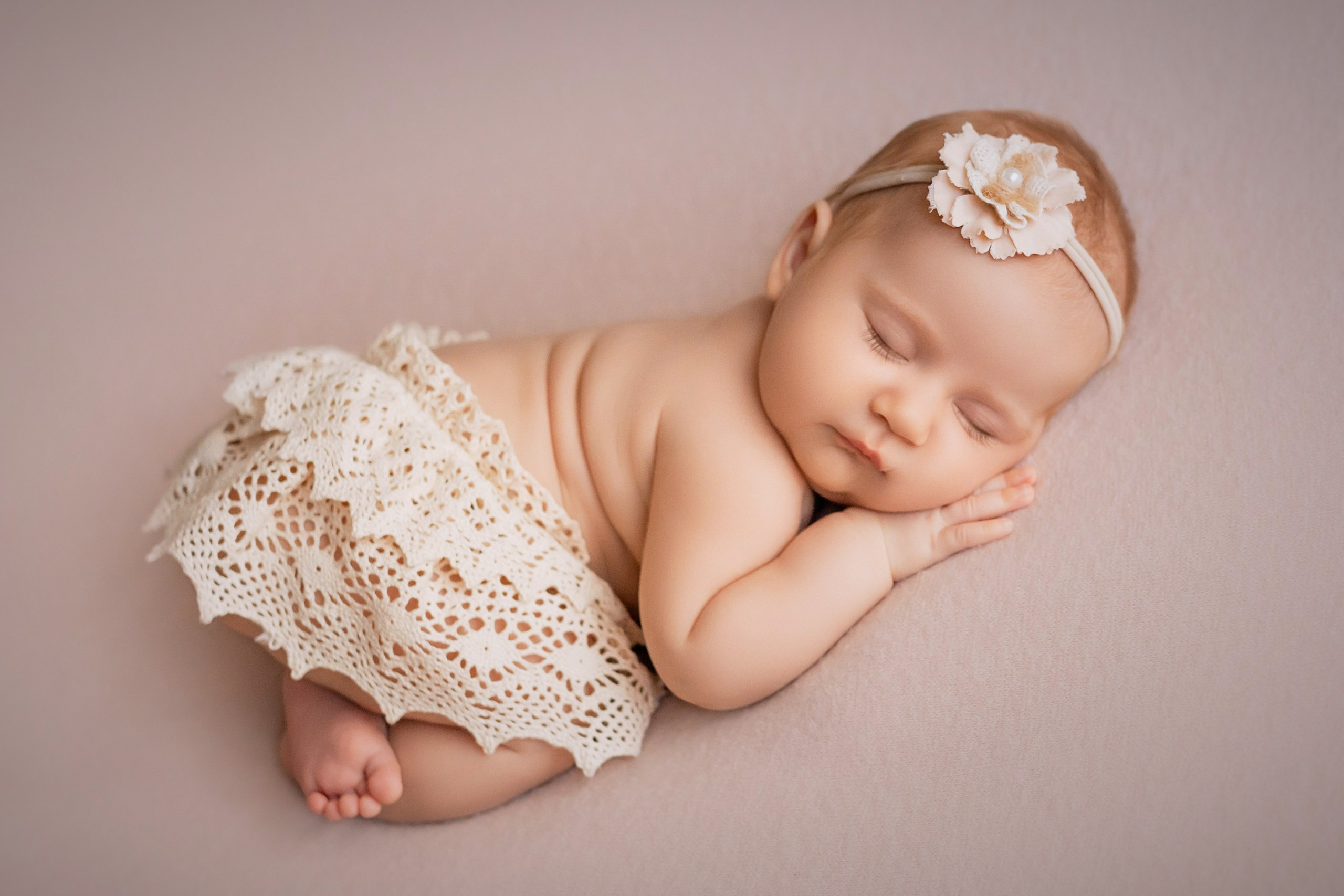 Newborn baby girl sleeping on tummy in lace skirt and headband
