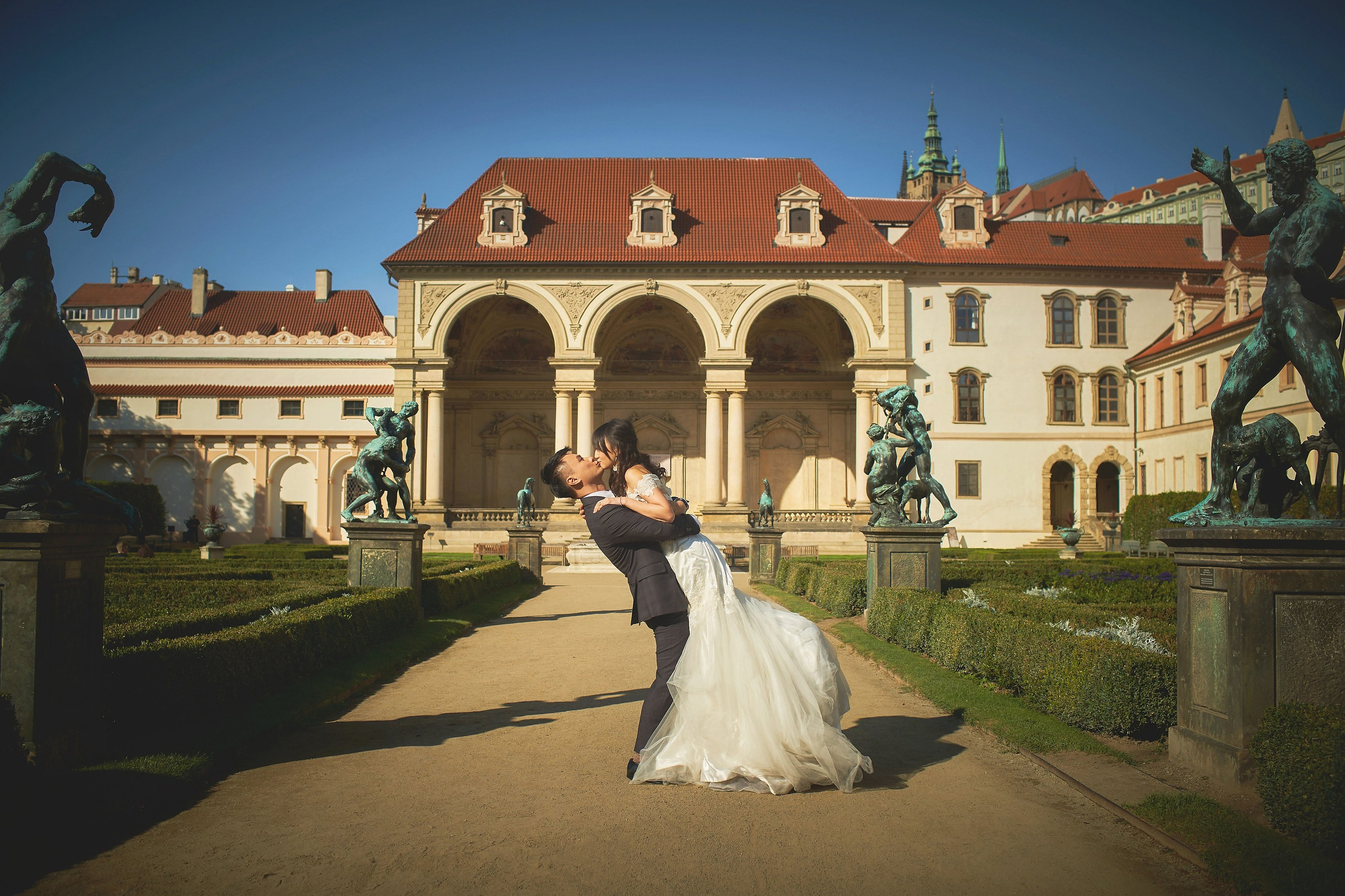 Groom Conan lifting and kissing bride Eva among the statues in Wallenstein Garden, Prague.