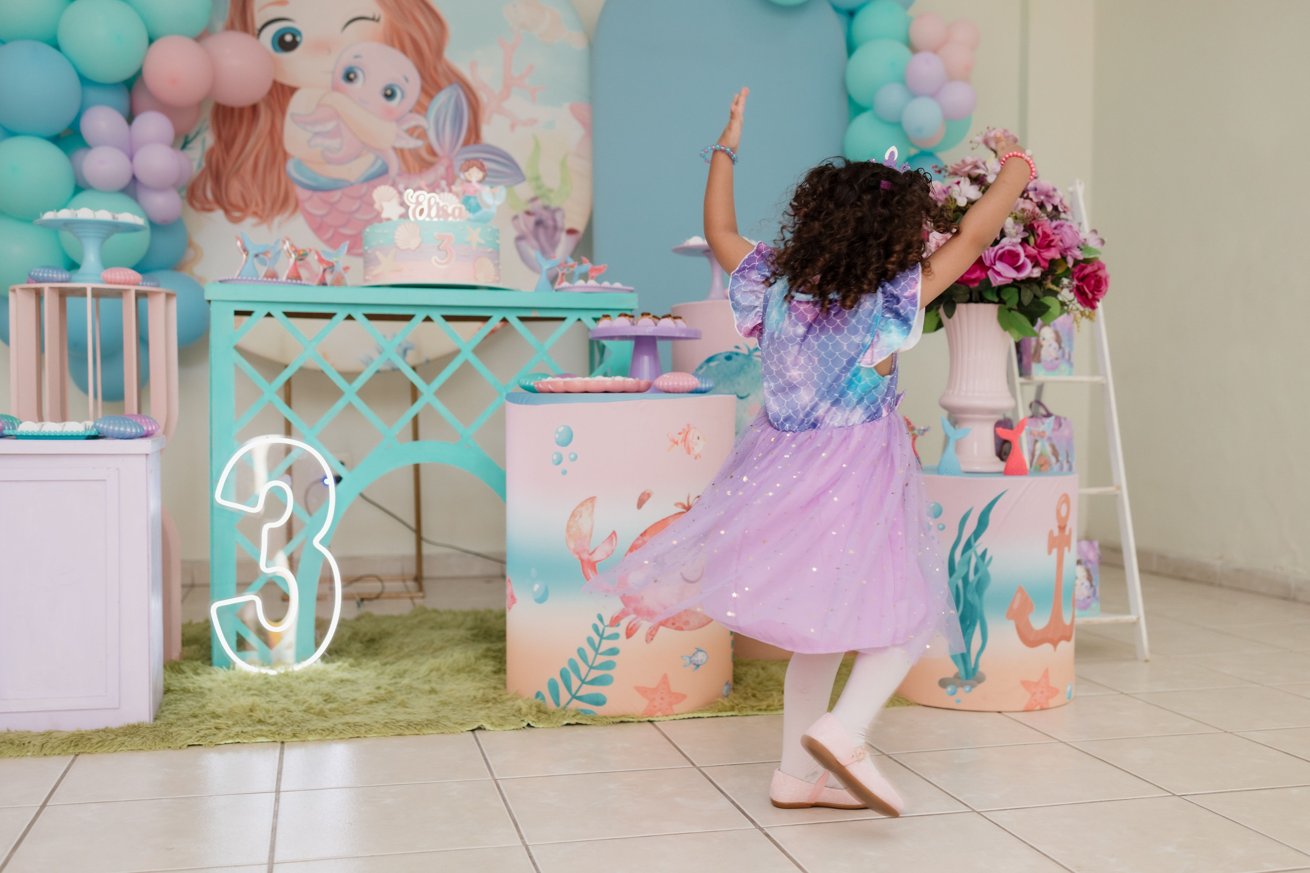 Elisa brincando de bailarina com roupa de sereia em frente a decoração da festa