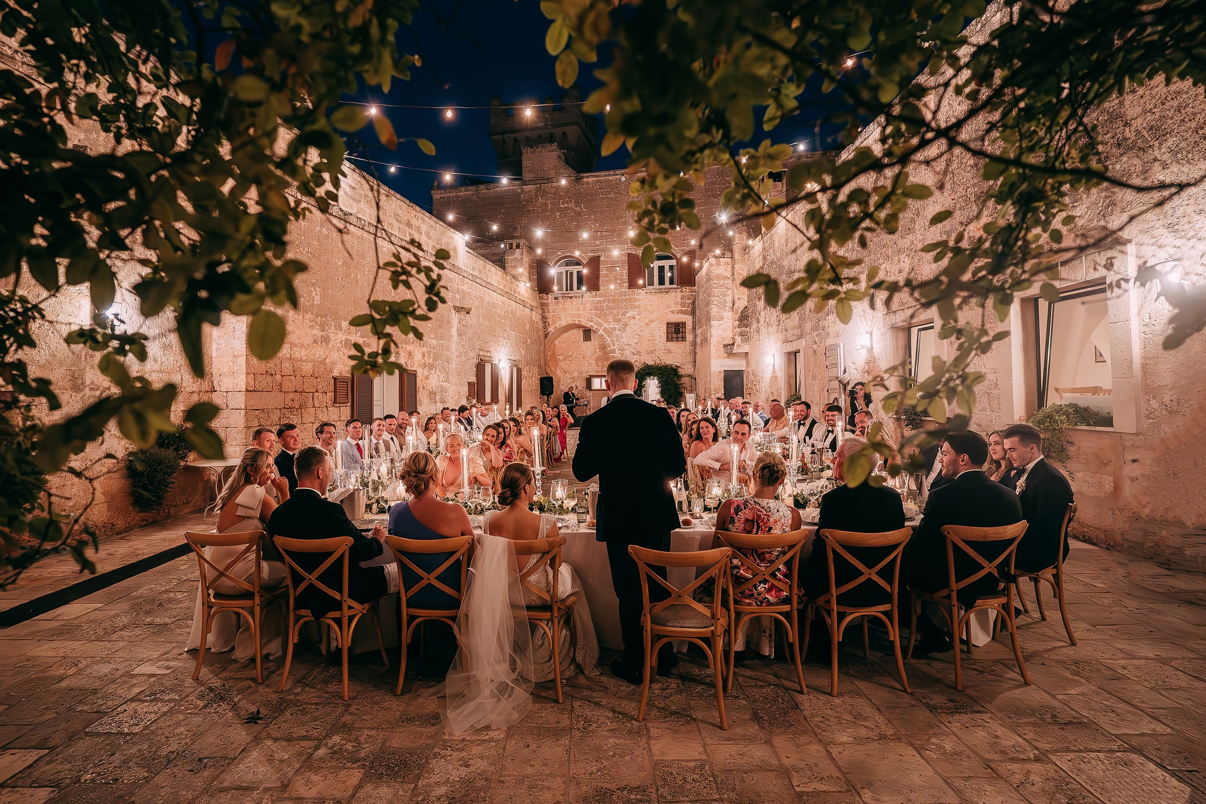 A newlywed couple shares a kiss surrounded by sparkling lights and bokeh, creating a magical evening ambiance.