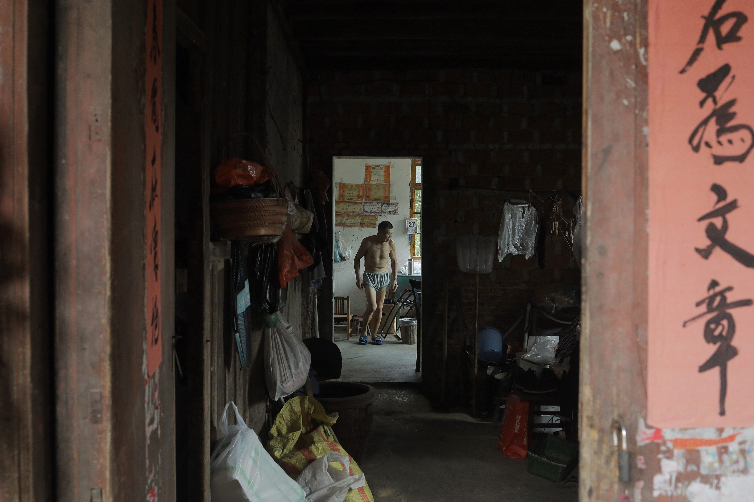 Yu Xueshun, 71, lives at his house with his wife in the village. The house built more than 80 years ago, even before the foundation of the PRC. A flood in the 1980s washed away some of the houses built in the same era. Yu Xueshun and his wife have one son and one daughter. Both of their children live in Hangzhou city and have two children each. Their daughter is planning to have a third child. Faded red couplets, traditional calligraphic inscriptions typically placed on doors during the Chinese New Year, are stuck on one doorway of Yu Xueshun's house. They once symbolized good fortune and prosperity.