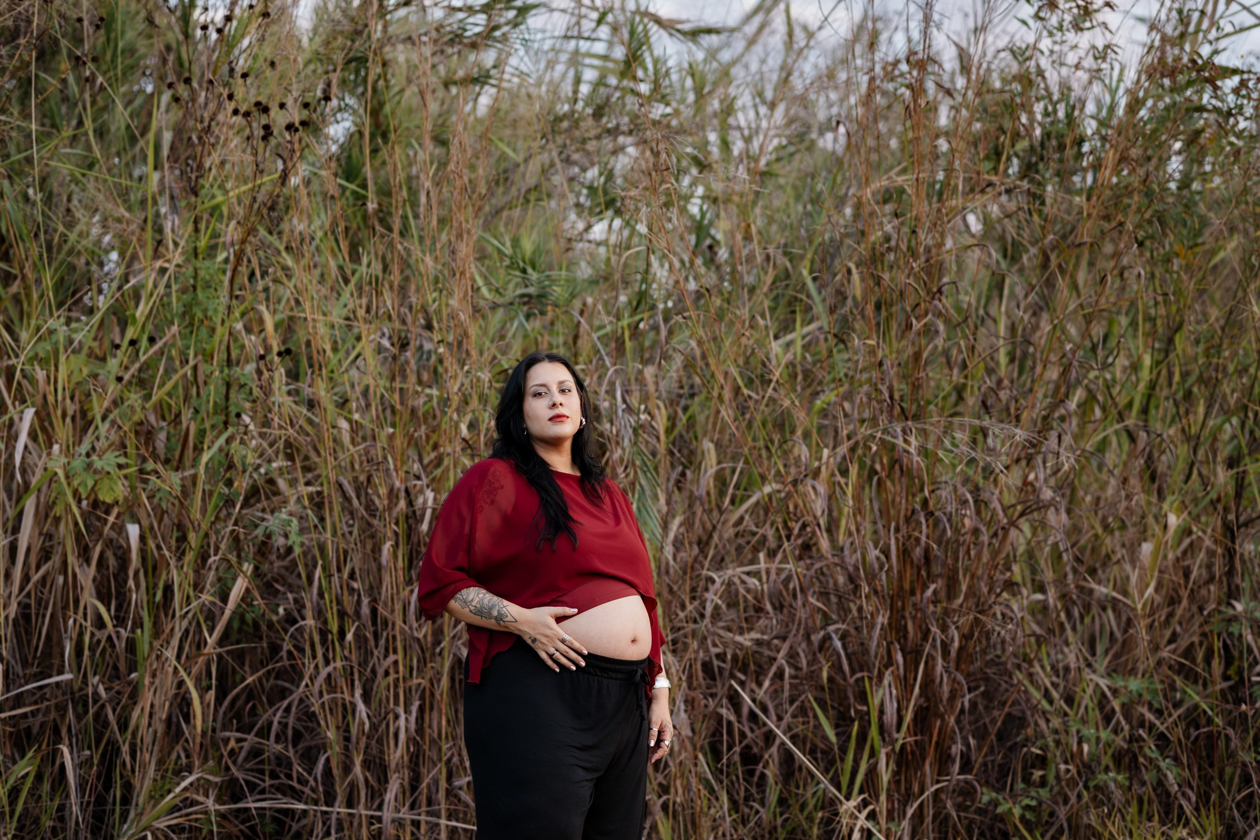 Mãe toca a barriga durante ensaio gestante ao ar livre.