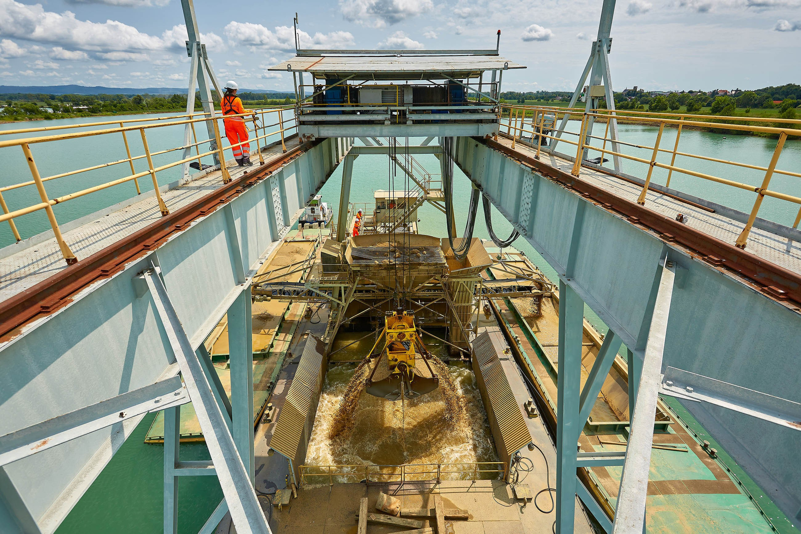 Workers look down over a pit as sediment is removed from the bottom of a lake by use of a large industrial-sized scooper.
