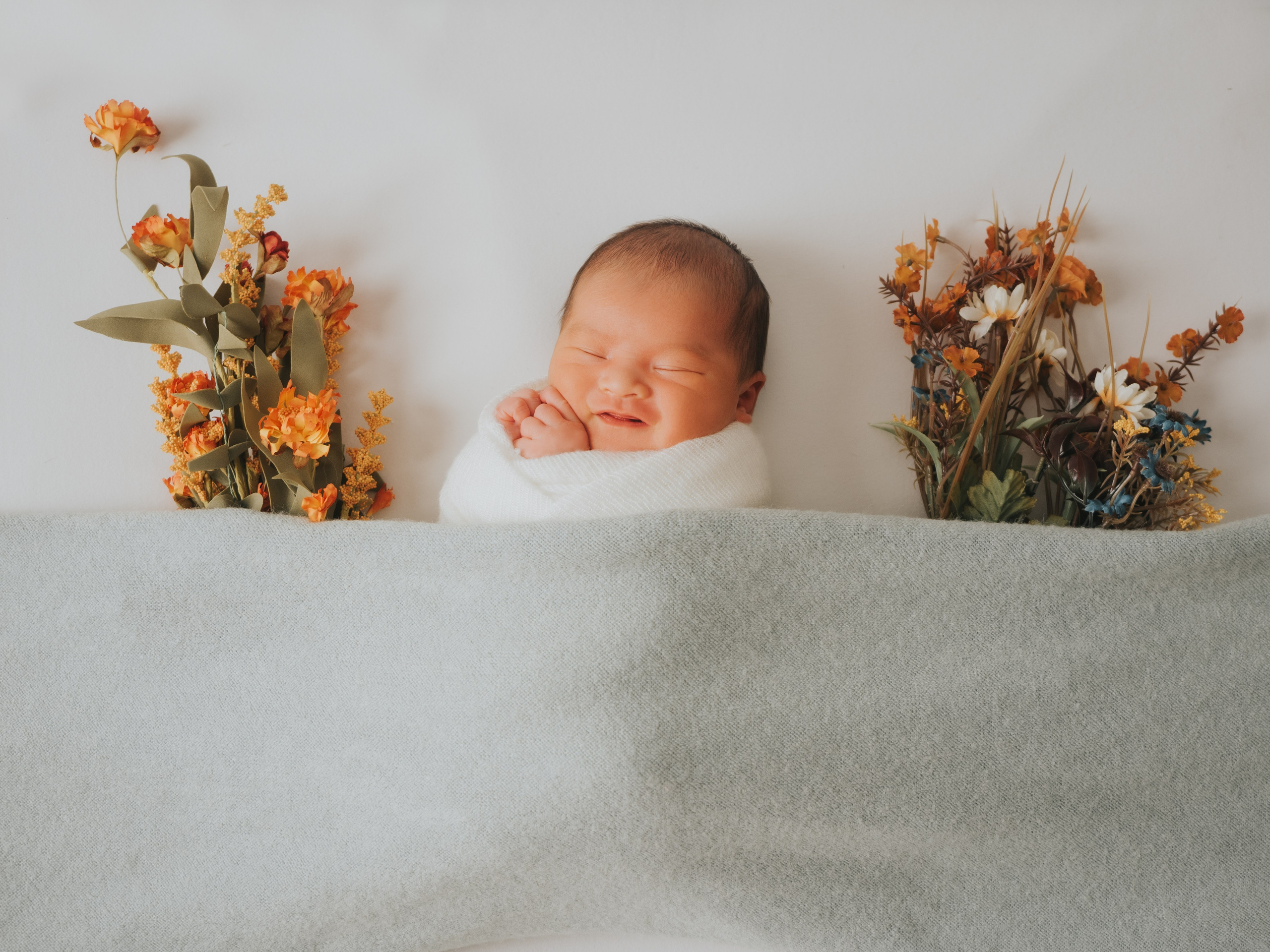 Newborn under blanket smiling with flowers around.