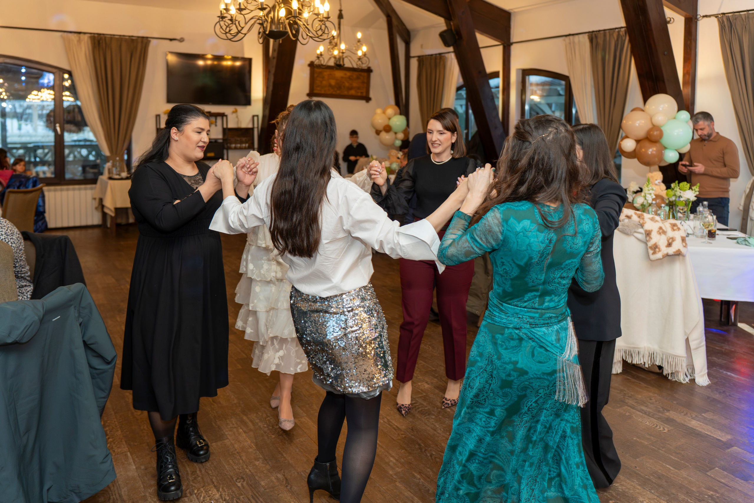 Group of women holding hands in a circle dancing indoors at an event.