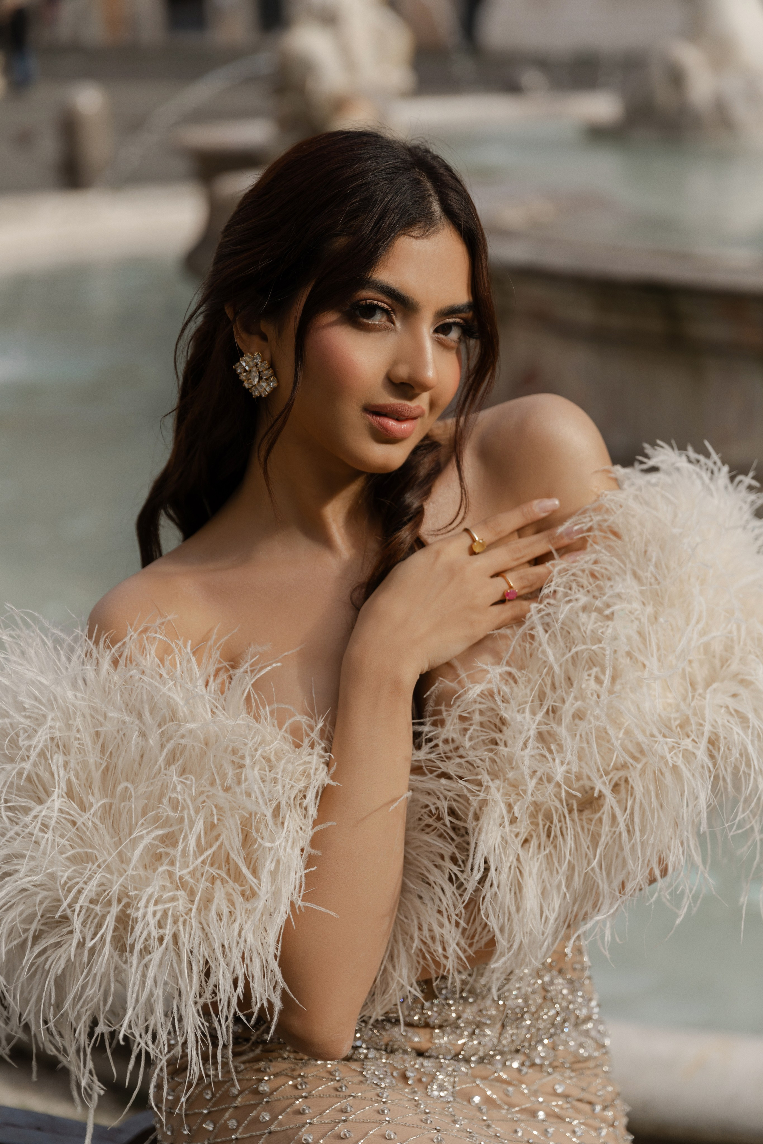 Indian girl in a wedding dress with a clean girl makeup and feathers sitting in front of a fountain