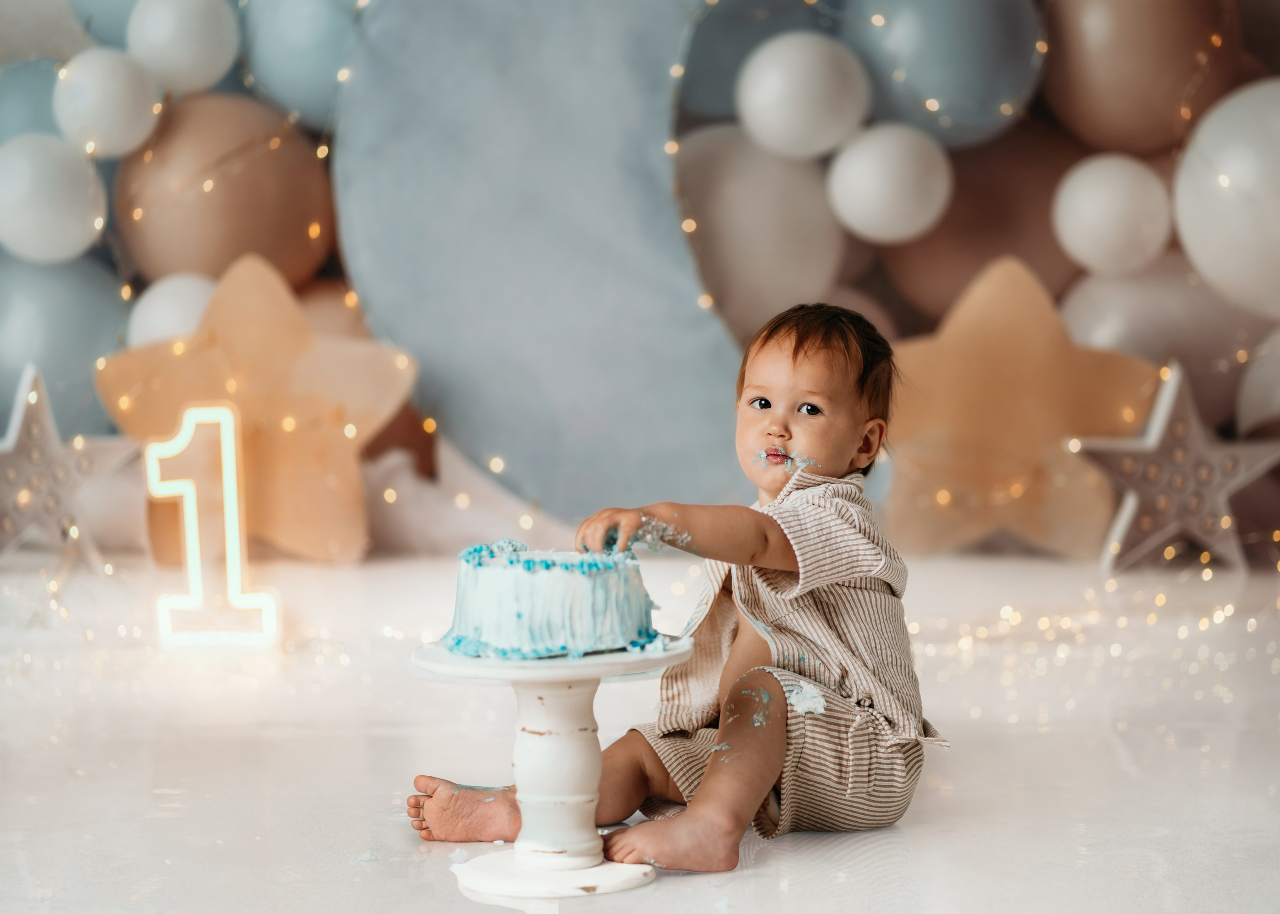 Beba sedi pored torte u plavoj dekoraciji sa lampicama, cake smash Beograd