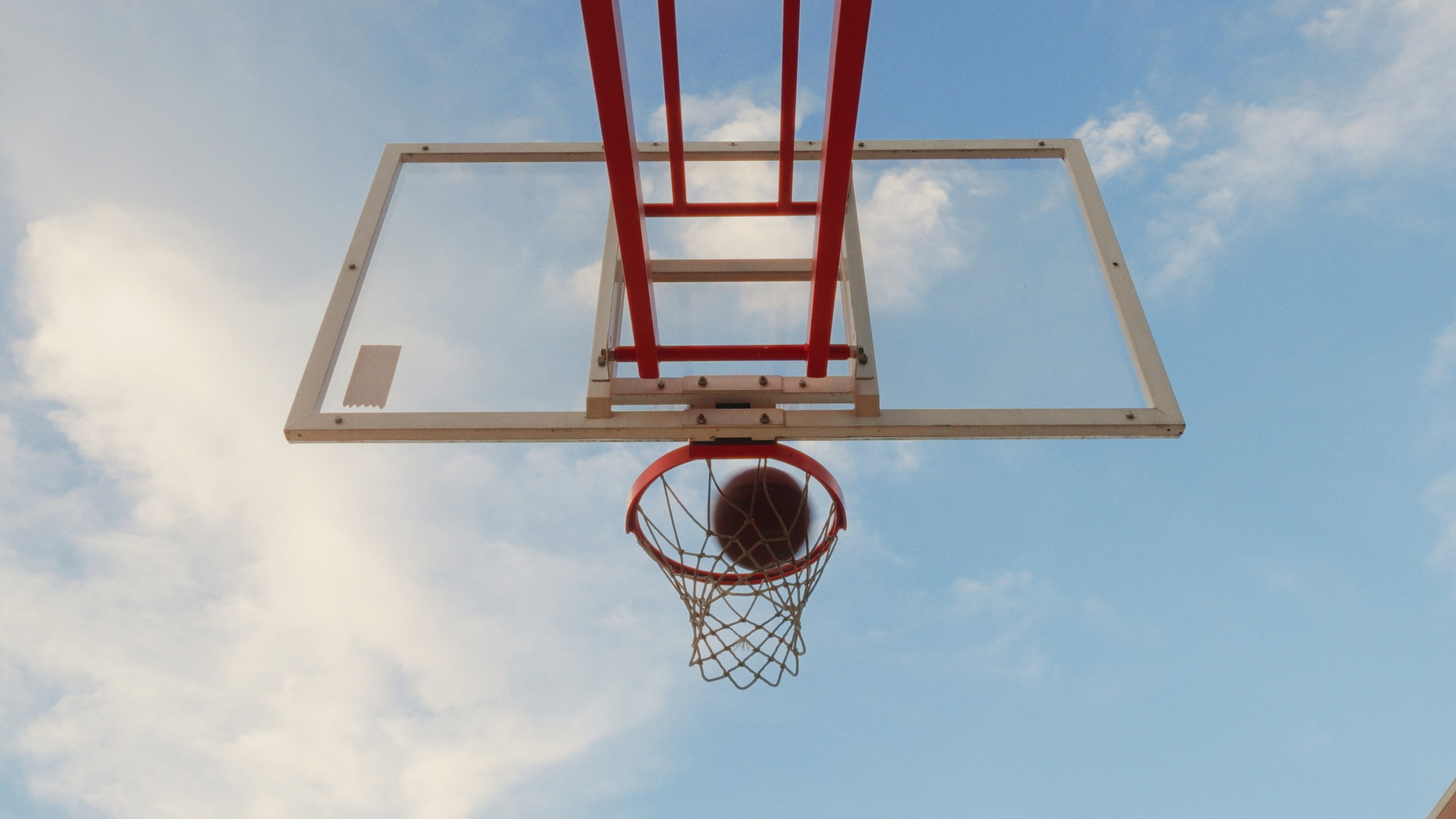 Fotografia desportiva em perspetiva vertical diretamente por baixo do cesto de basquetebol contra o céu, captada pela Khave Media