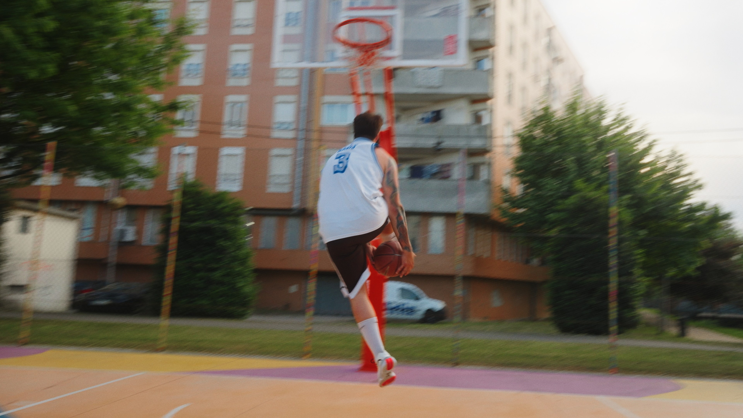 Fotografia dinâmica de basquetebol de rua com um jogador a saltar em direção ao cesto num campo urbano, produzida pela Khave Media