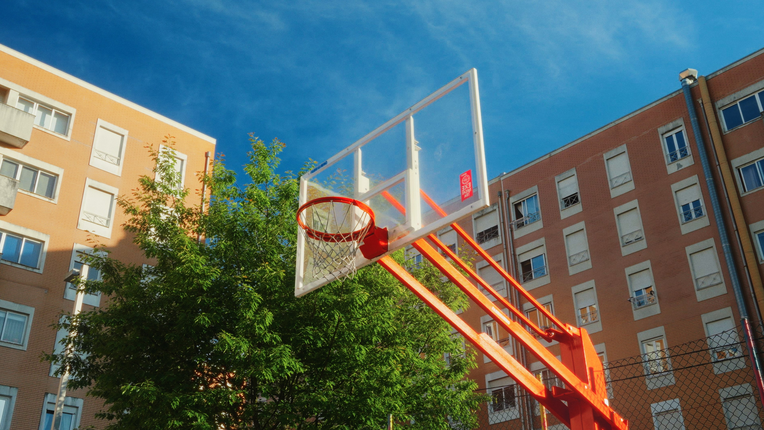 Fotografia desportiva urbana num ângulo contrapicado de uma tabela de basquetebol de rua com edifícios ao fundo, produzida pela Khave Media
