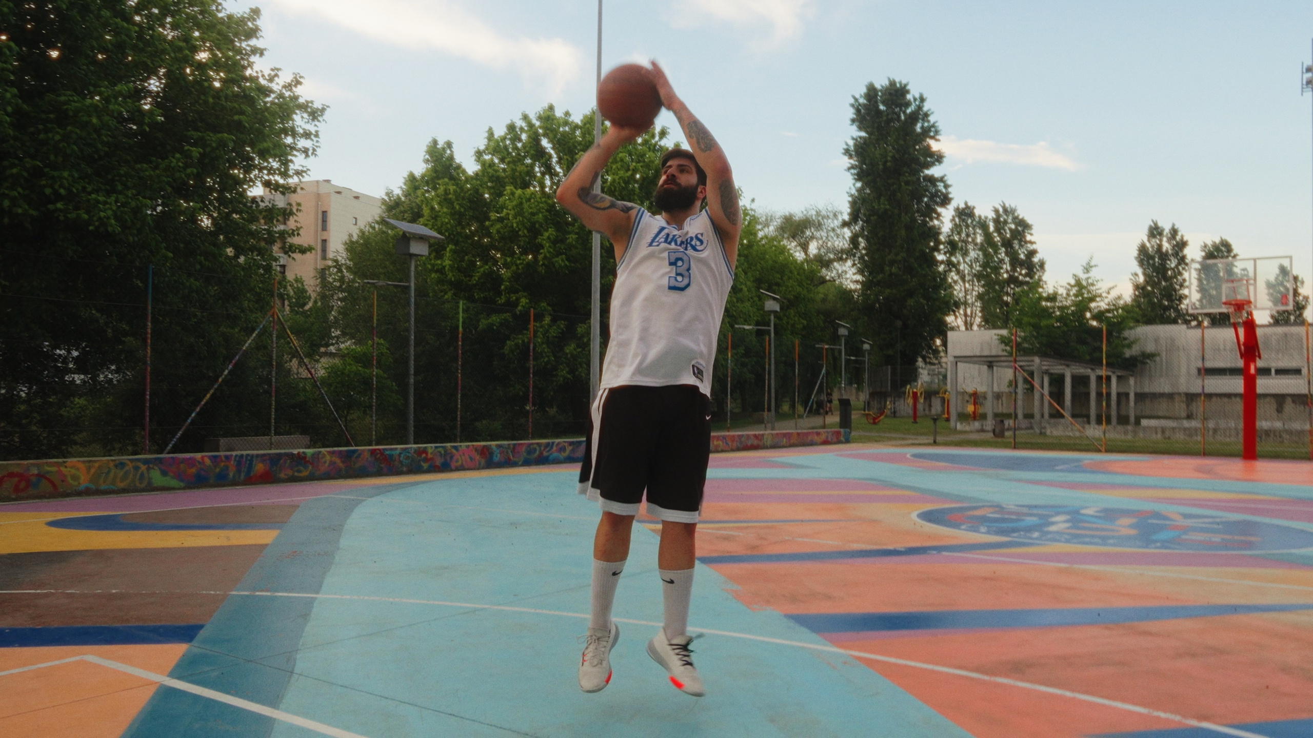 Fotografia de ação desportiva de um jogador de basquetebol a fazer um lançamento em suspensão num campo exterior, pela Khave Media