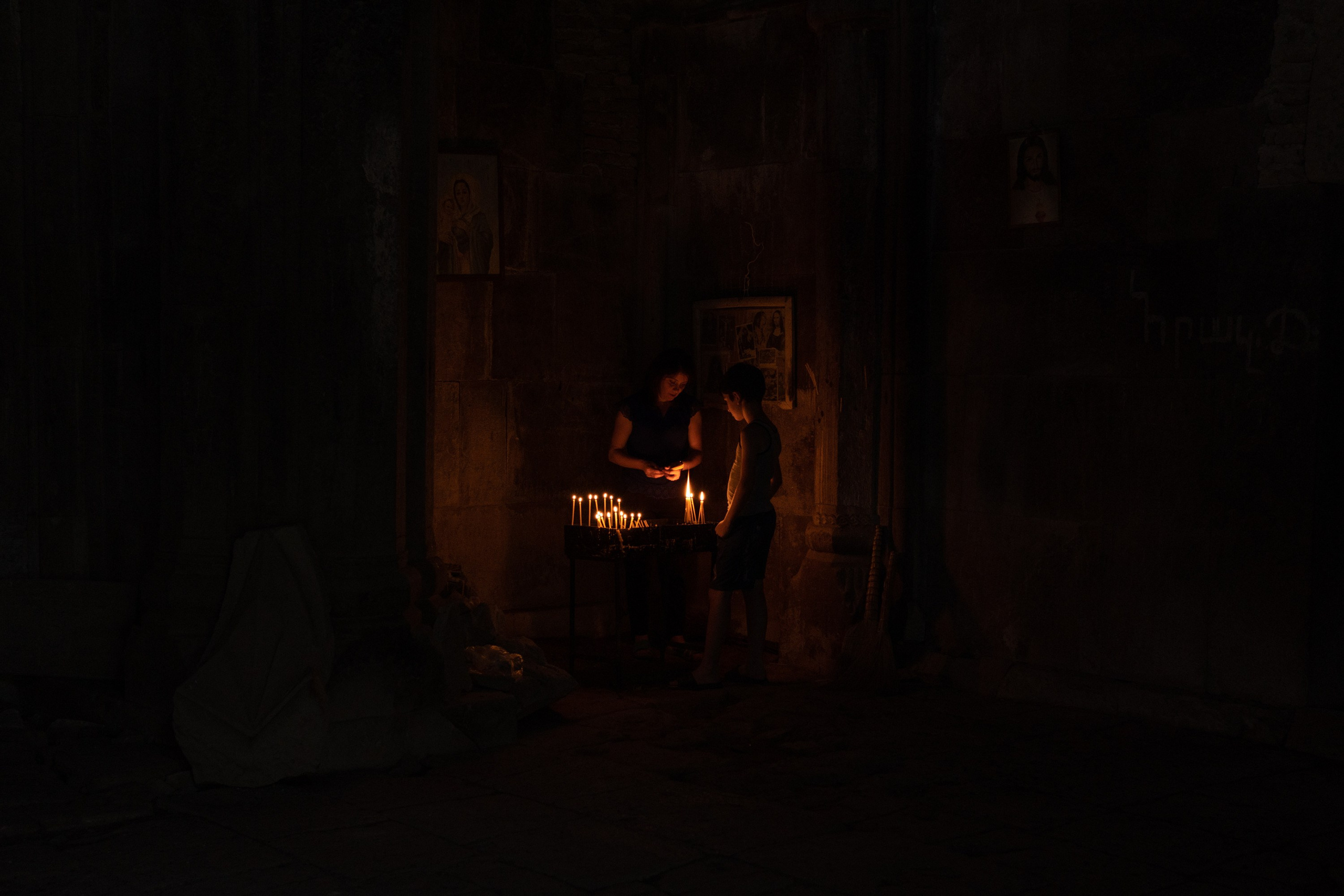 Lusine (left) and her son (right) - who live in the border village of Aygedzor - are lighting candles and praying for health and peace in the abandoned Khoranashat monastery (13th century). They traveled a dangerous road to get there. The last time Lusine visited the monastery was in the 1990s.