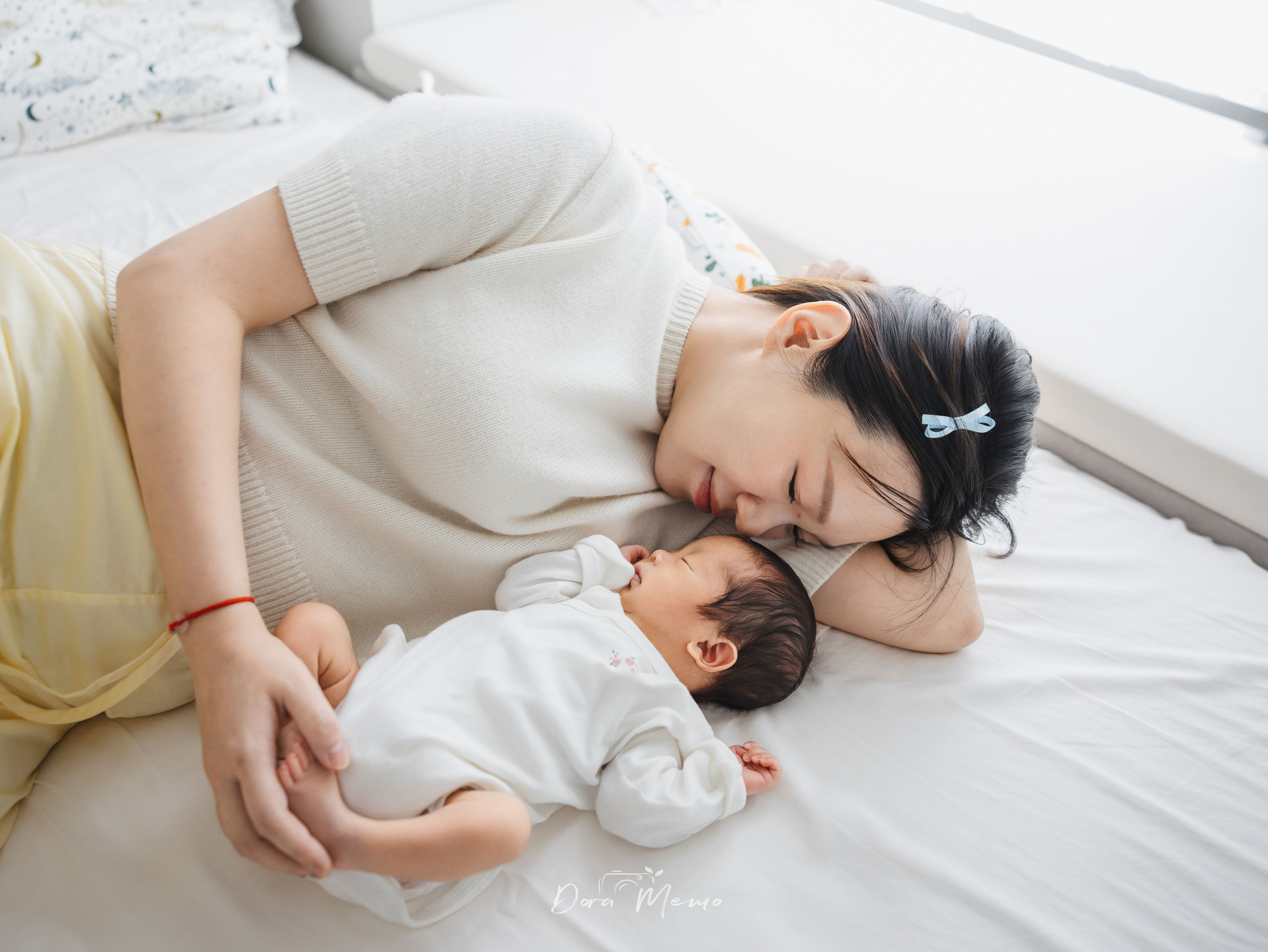 Mother lying beside her newborn, face pressed gently against the baby's head, tender moment of maternal love