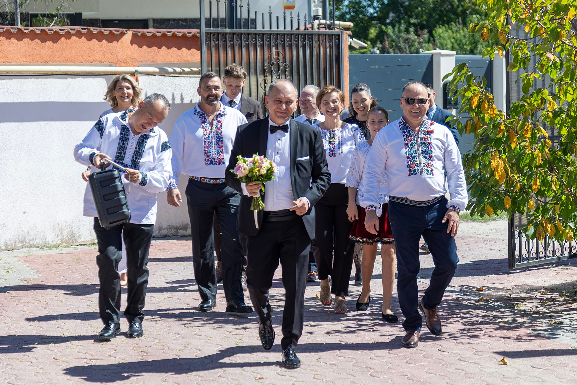 Mirele cu buchetul și invitații îmbrăcați în ii tradiționale merg la naș acasă