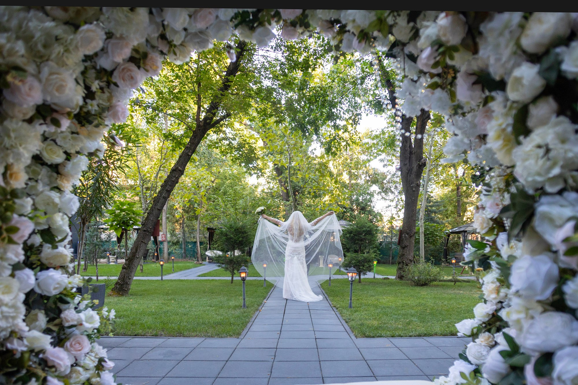 Mireasa cu voalul lung fotografiat prin arcada florală la Baroque Events & Garden București